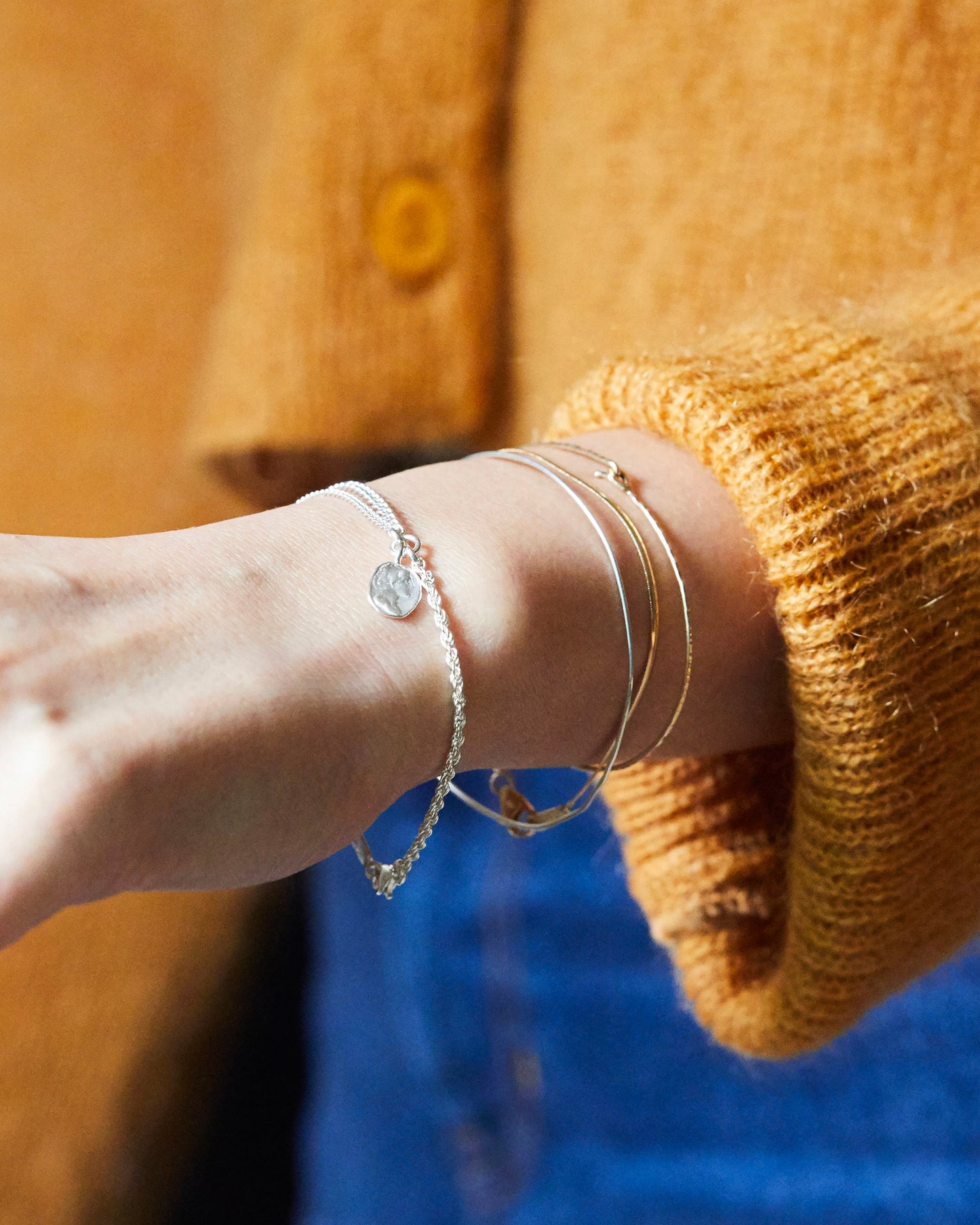 Minimalist silver bracelet with handcrafted coin charm, worn on wrist with layered bangles