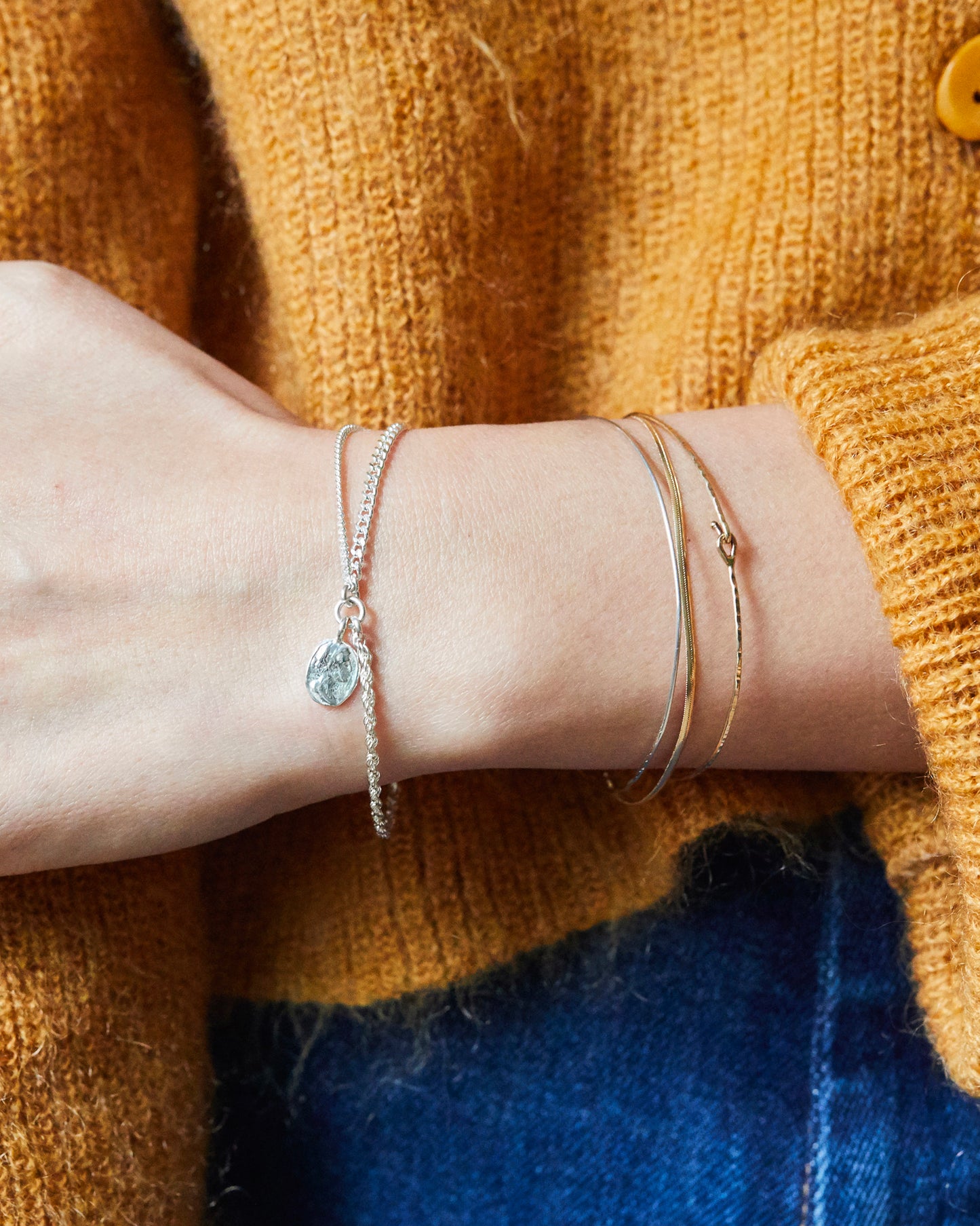 Hand wearing B507 silver bracelet with hammered coin charm, styled with cozy knitwear