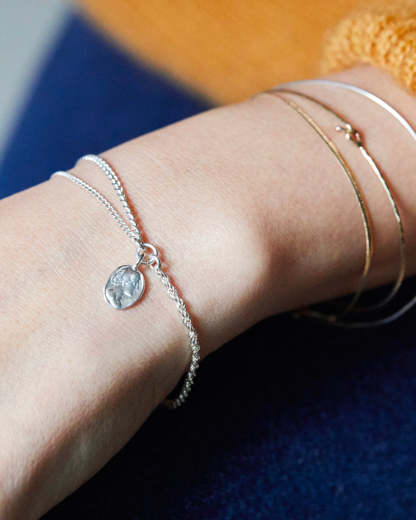 Silver charm bracelet worn on wrist, styled with mixed-metal bangles and mustard sweater