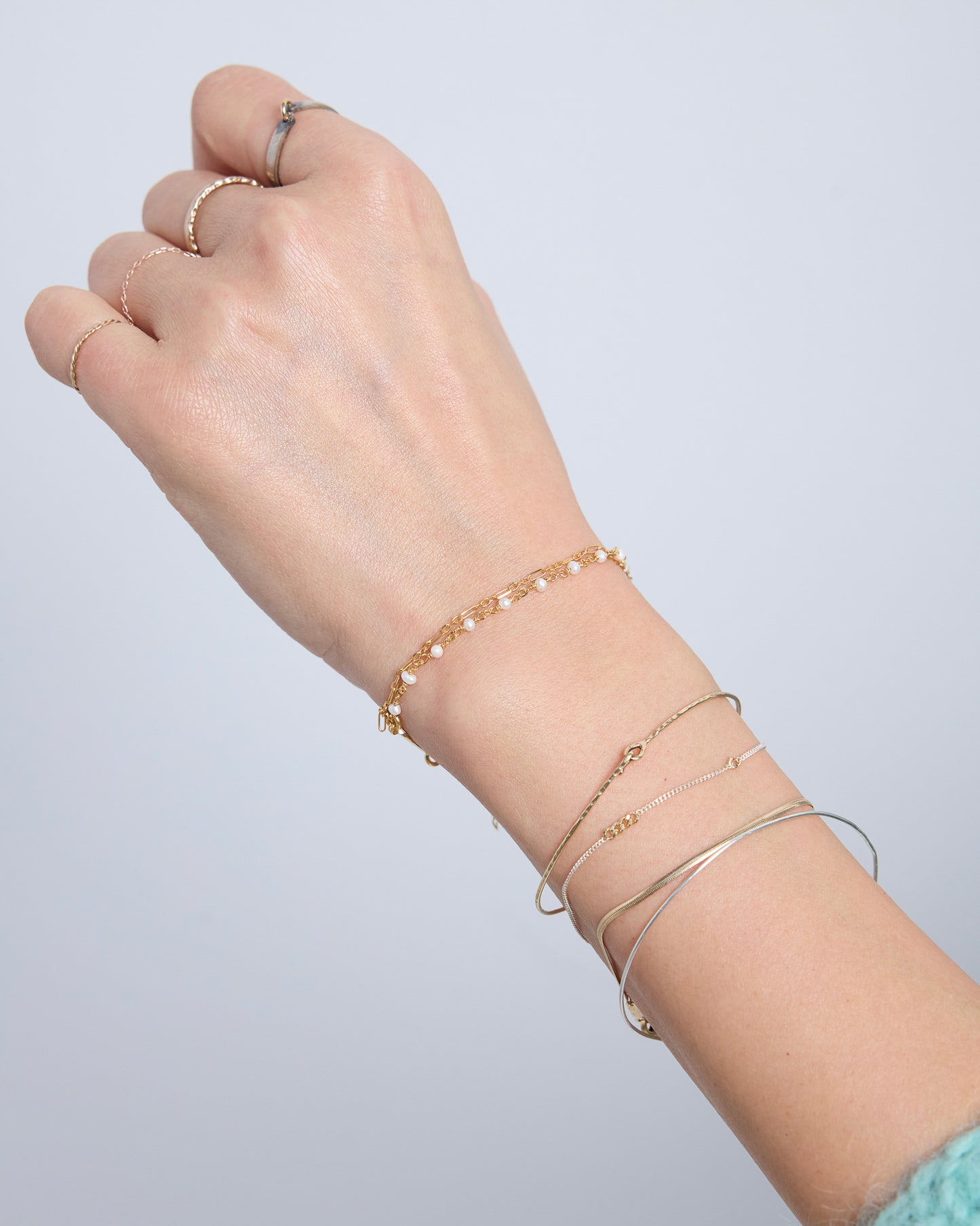 Delicate double layered pearl bracelet in gold worn on wrist with cozy knit sweater, minimalist everyday jewelry styling