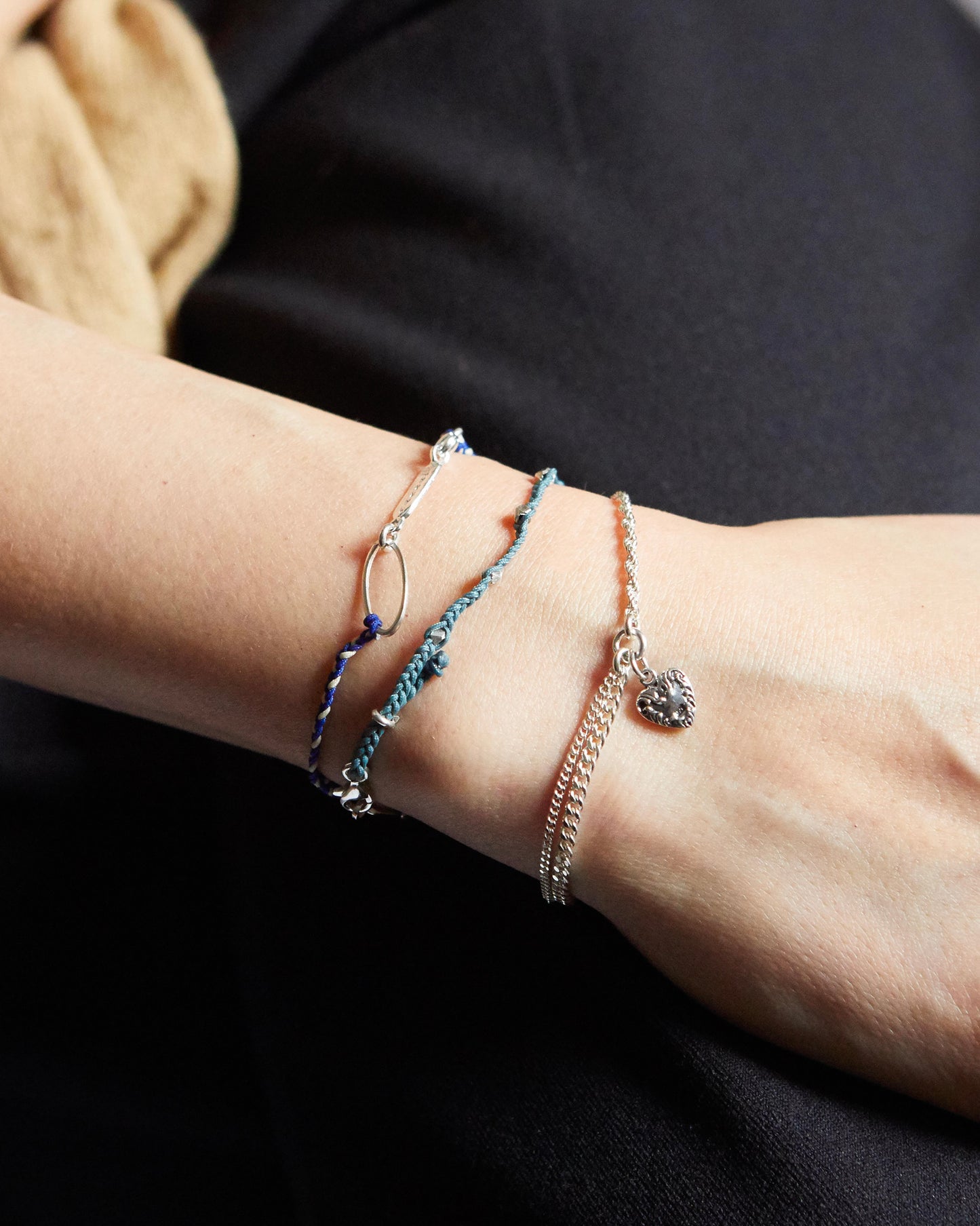 Layered bracelet styling featuring red and silver strands, with heart charm as focal piece