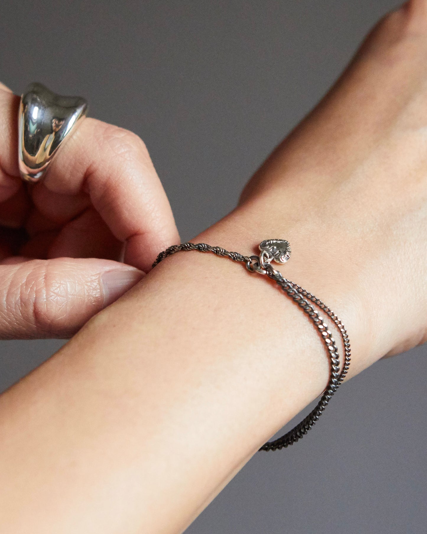 Close-up of a wrist wearing a bracelet with a heart charm, against a neutral background.