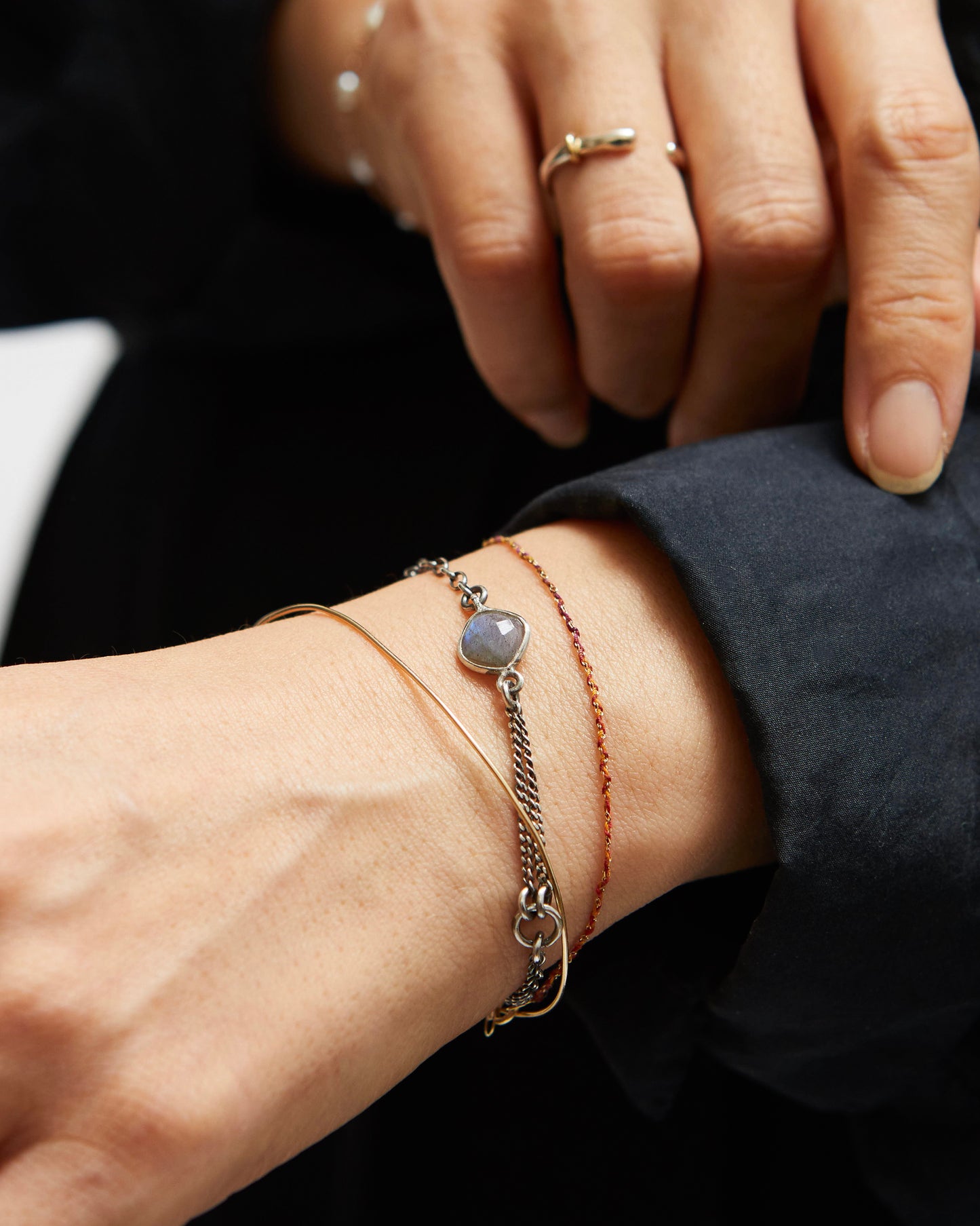 Close-up of a wrist with multiple bracelets and a ring on a dark background