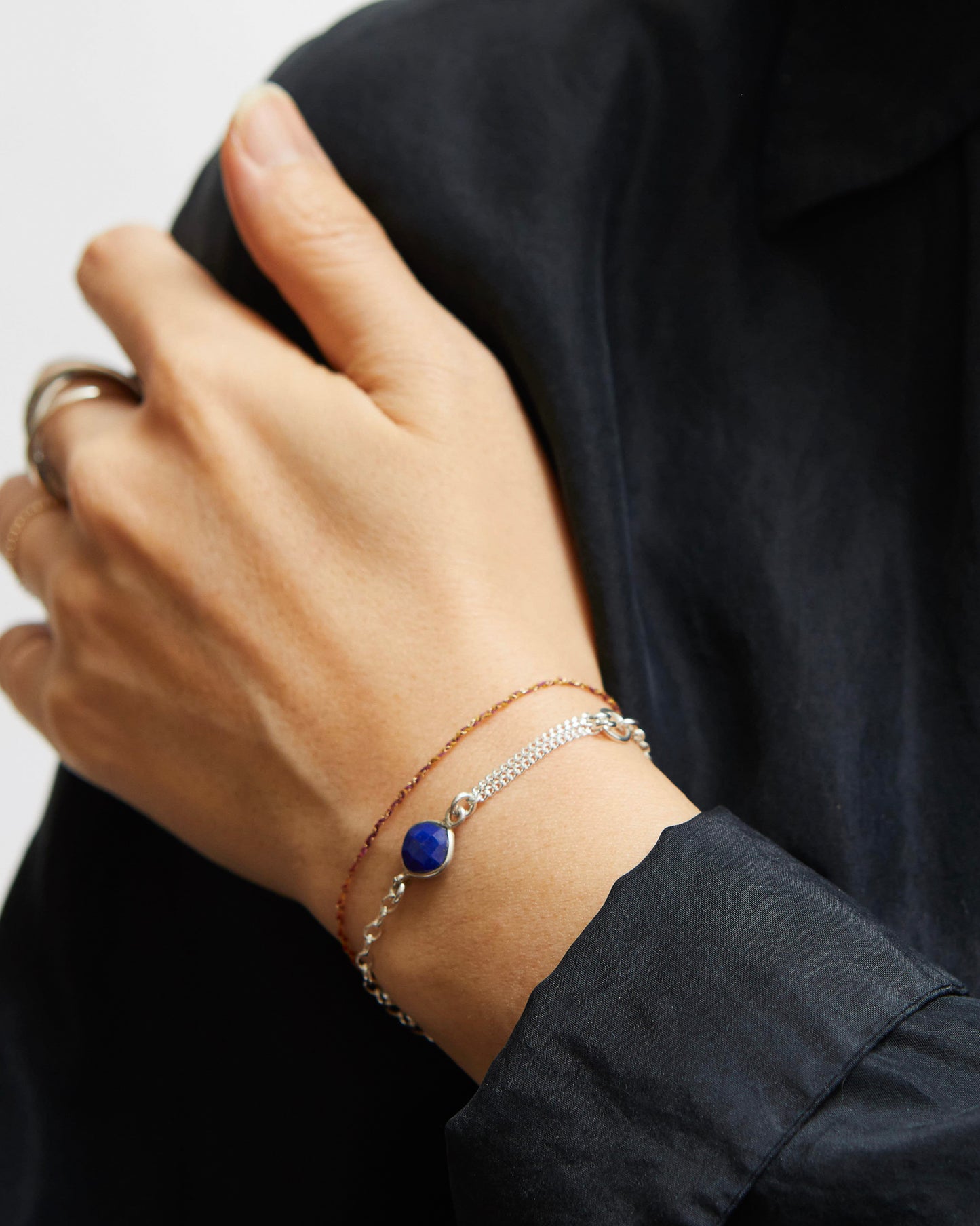 Close-up of a hand wearing two bracelets with a dark shirt background