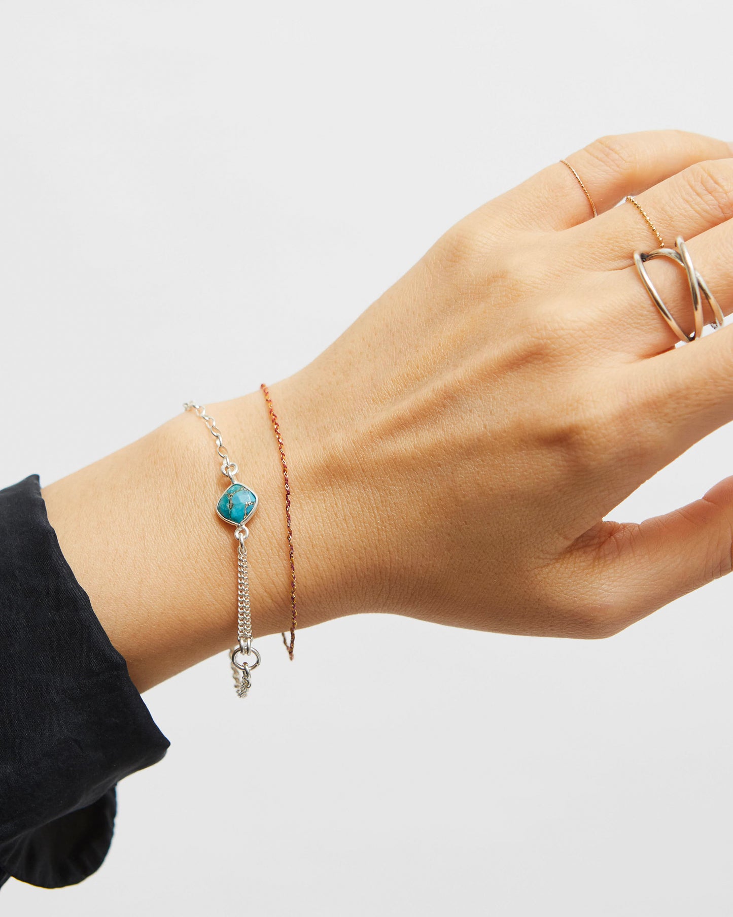 Hand wearing a silver bracelet with a turquoise charm on a plain background