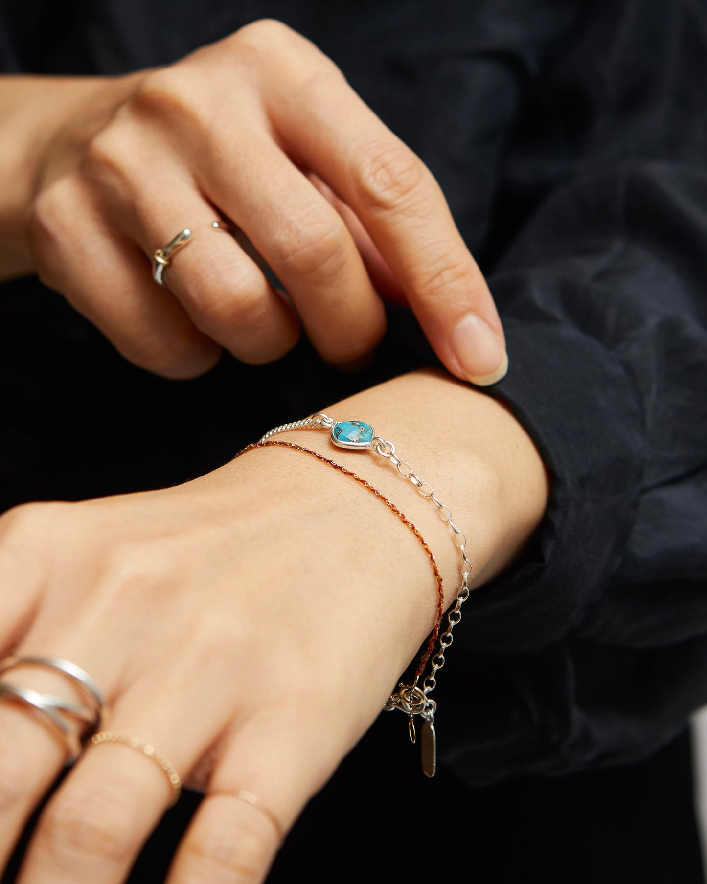 Close-up of a hand wearing multiple bracelets and rings on a black background