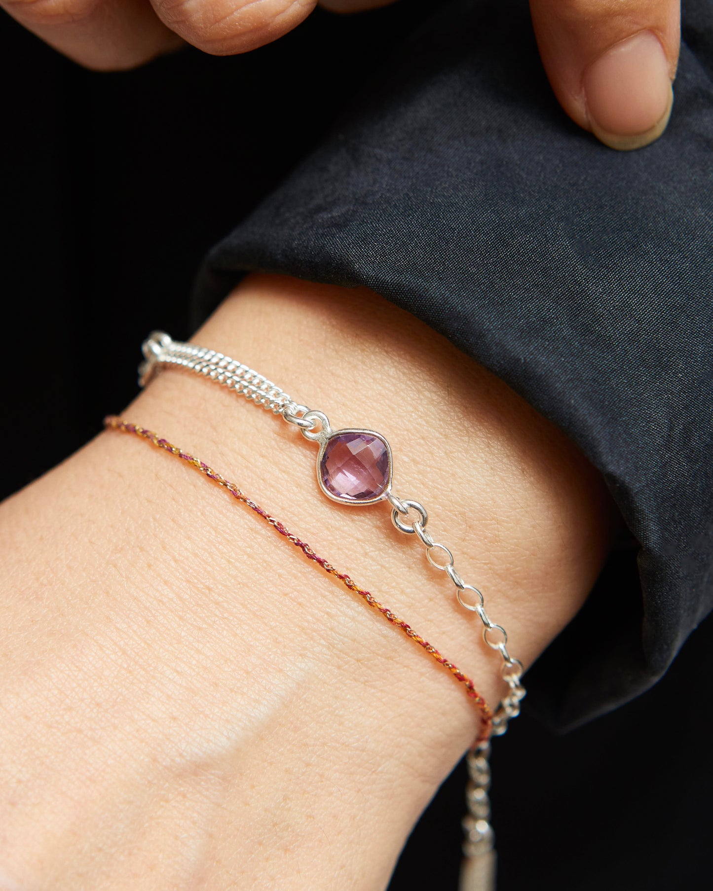 Silver bracelet with an amethyst gemstone on a wrist against a dark background