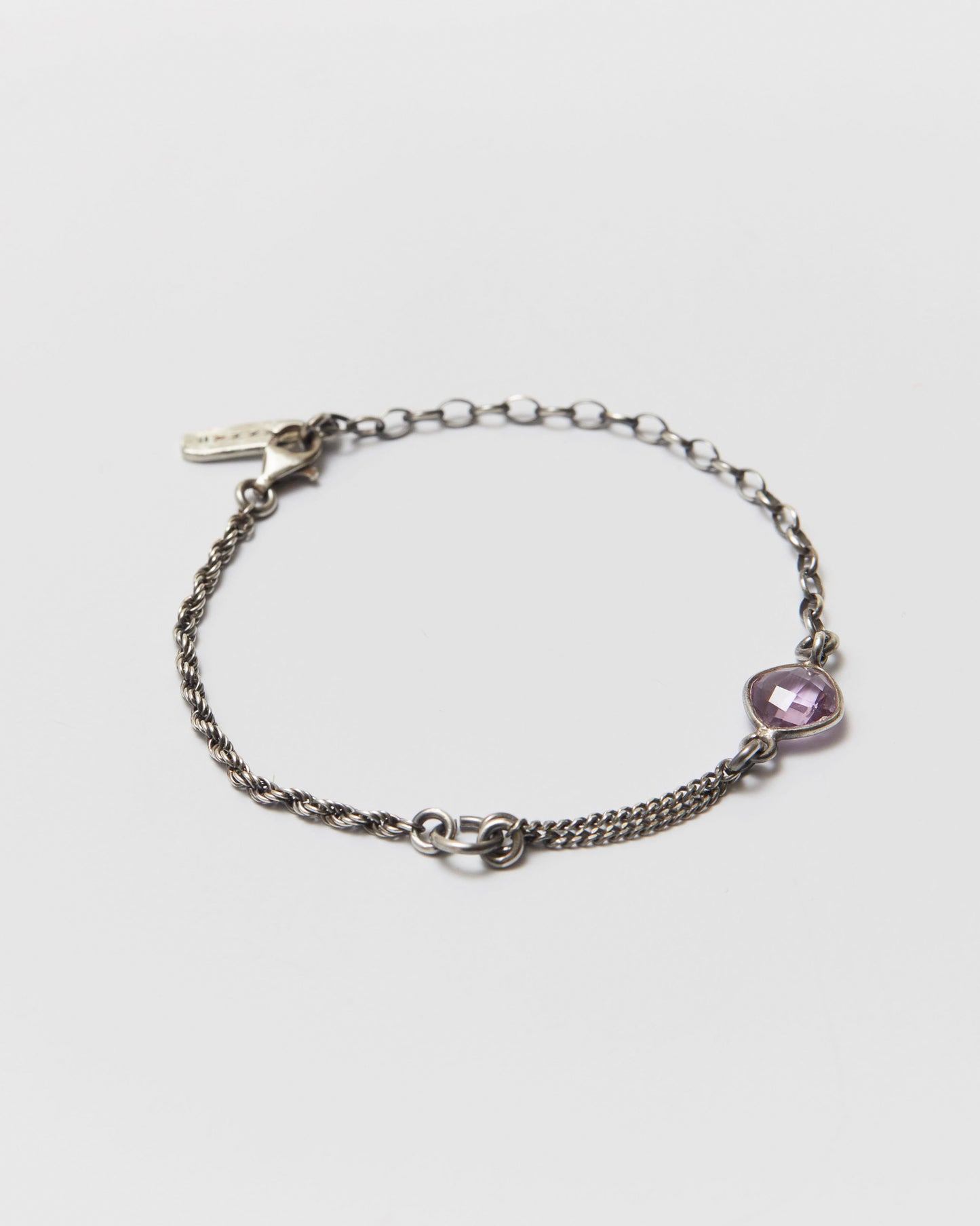 antique silver chain bracelet with a an amethyst charm on a light gray background