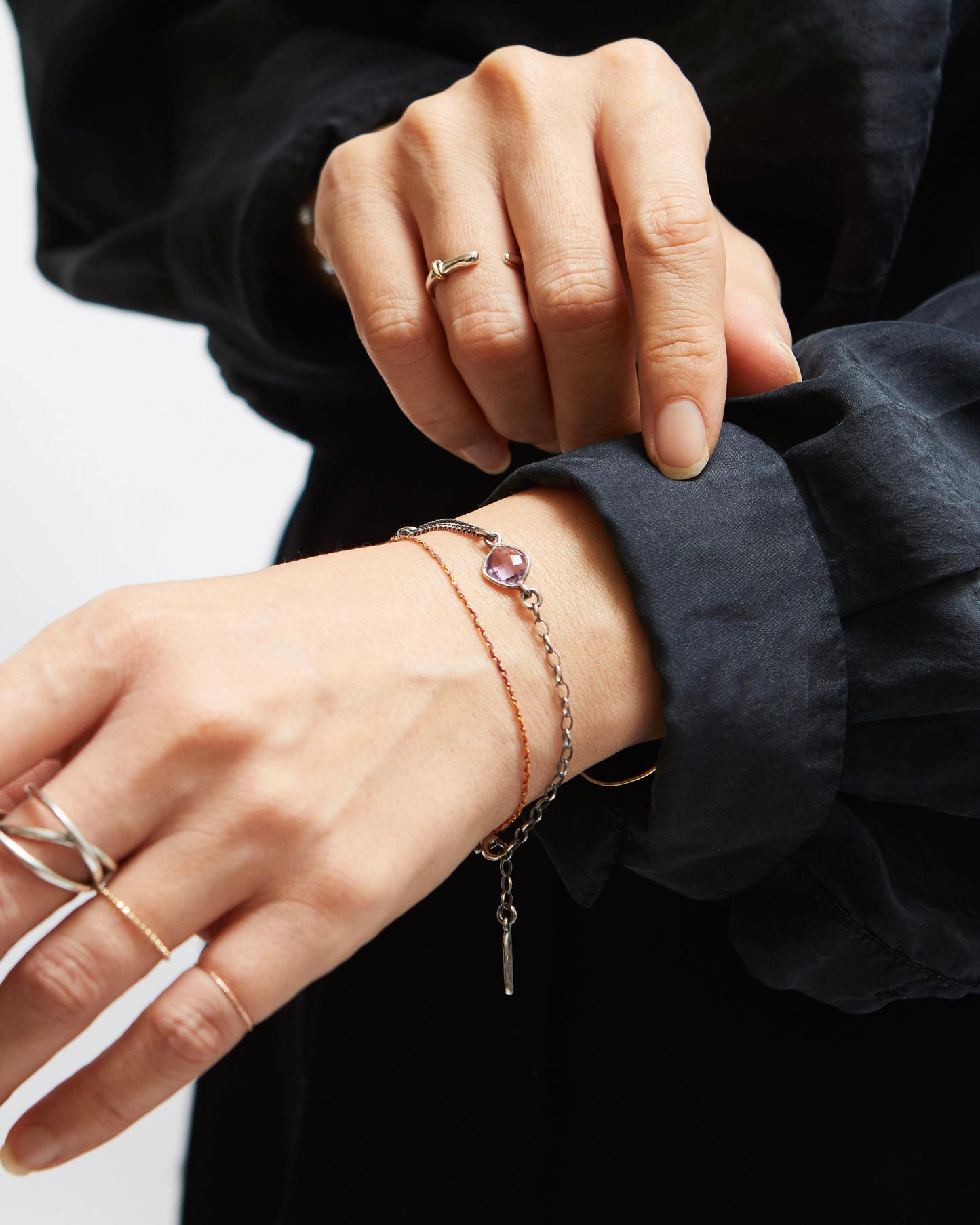 Close-up of a hand wearing multiple bracelets and rings with a black sleeve.