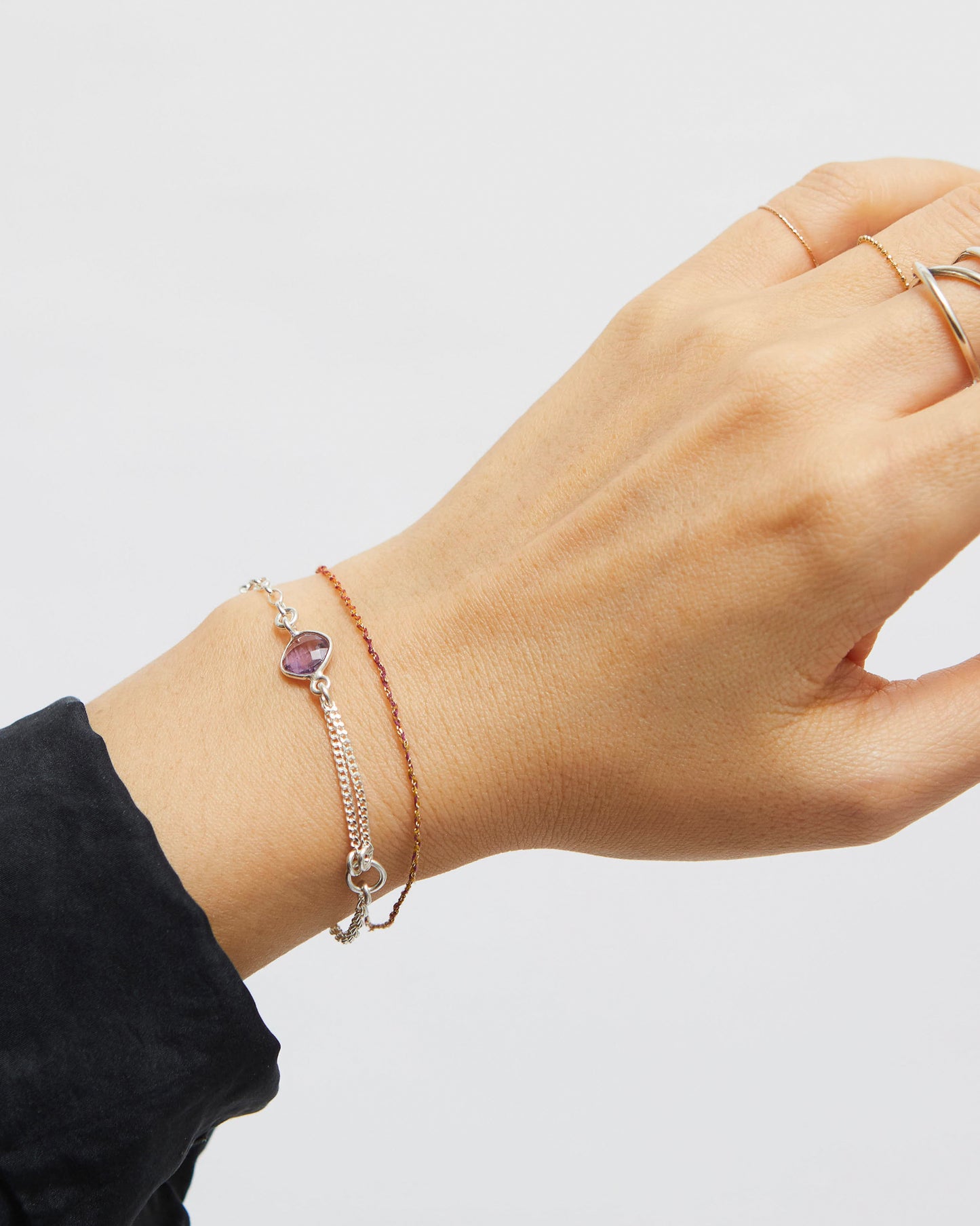 Hand wearing a silver bracelet with an amethyst gemstone on a plain background