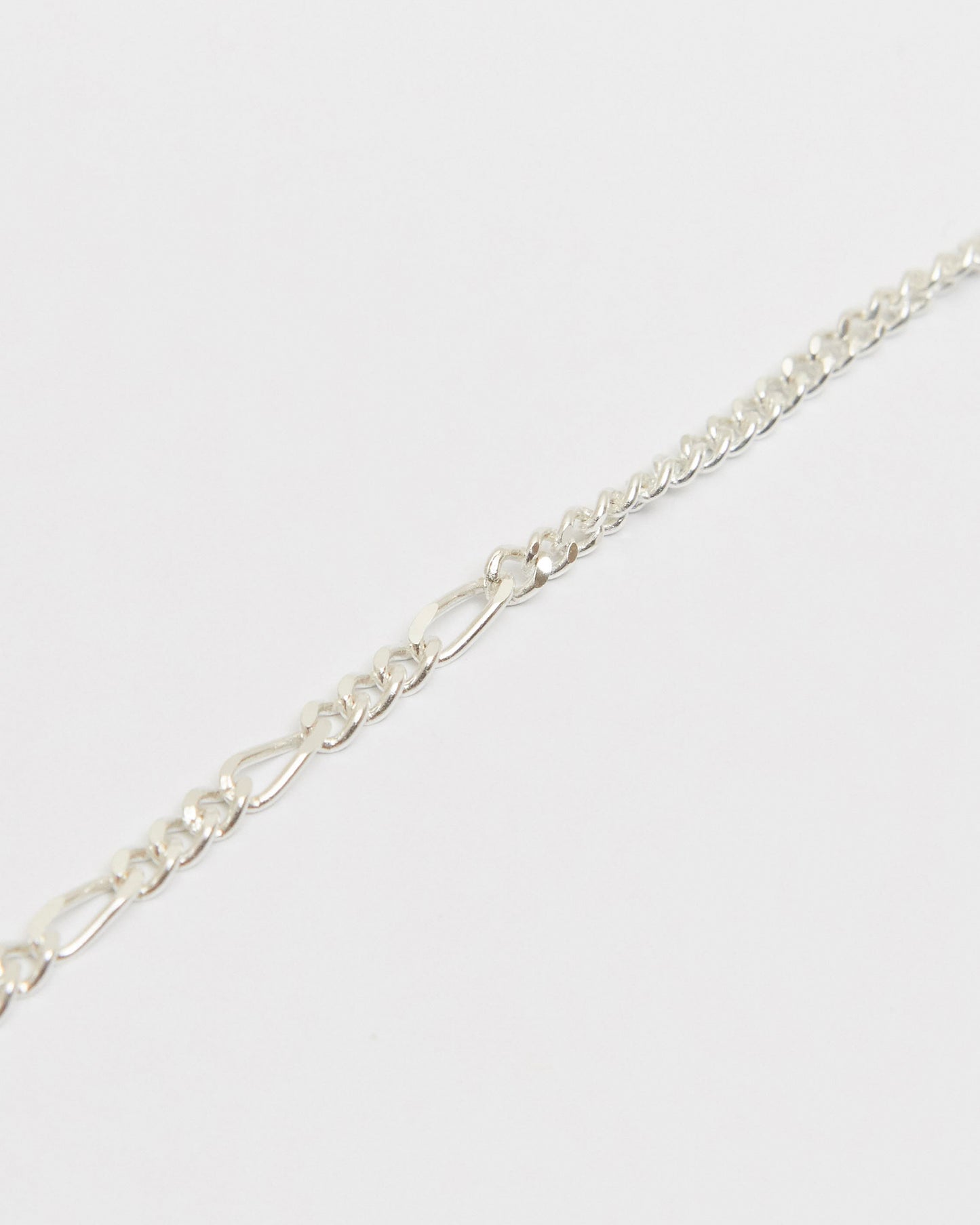 Macro close-up of sterling silver mixed chain bracelet highlighting polished curb chain texture and elongated link details.