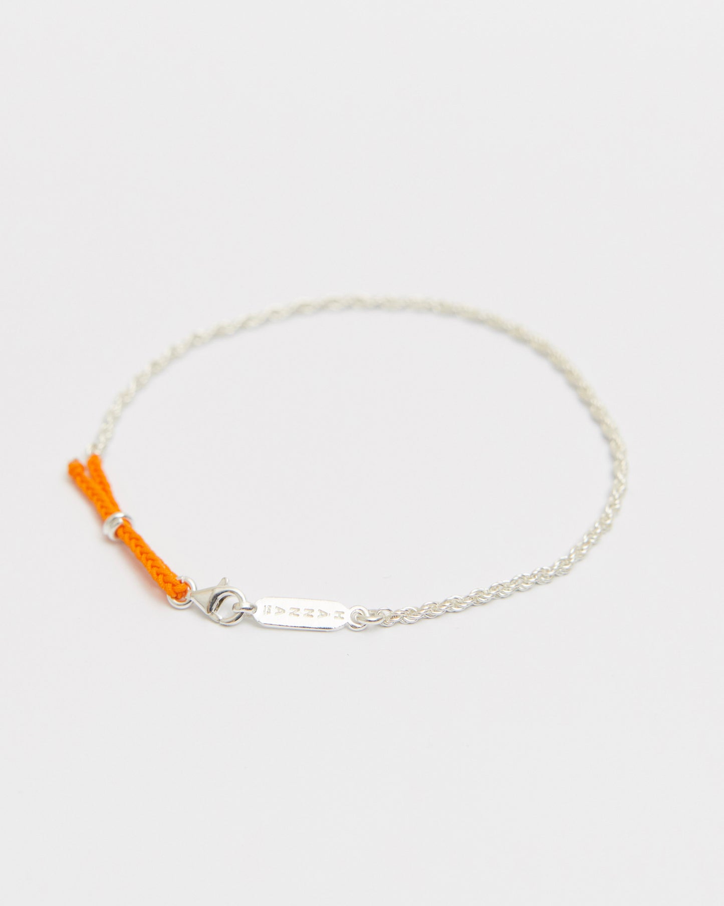 Minimal sterling silver bracelet with bright orange braided cord detail and delicate chain on white background.
