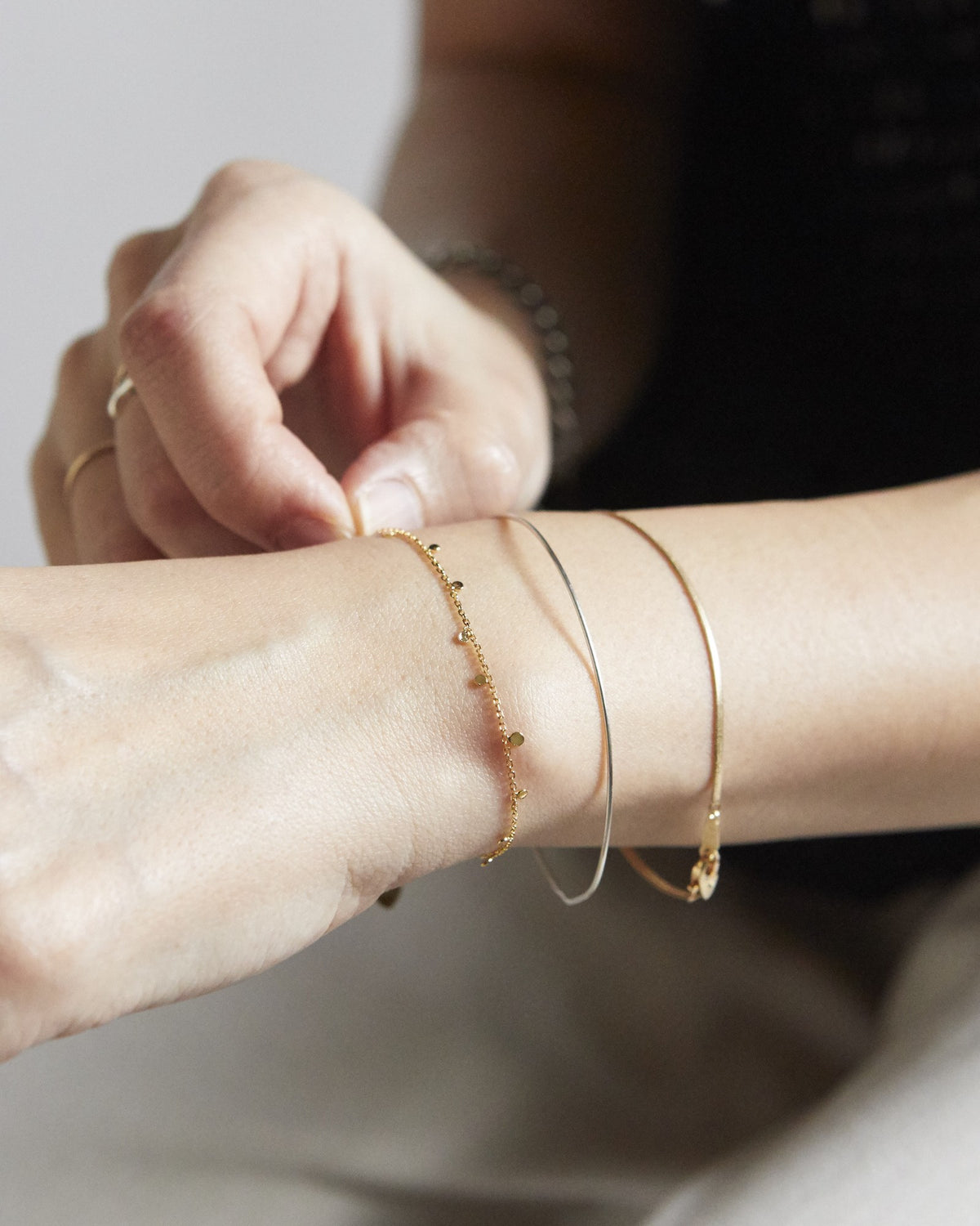 Hand adjusting a gold dot chain bracelet layered with thin bangles – HANNA543 B96 dew drop garland