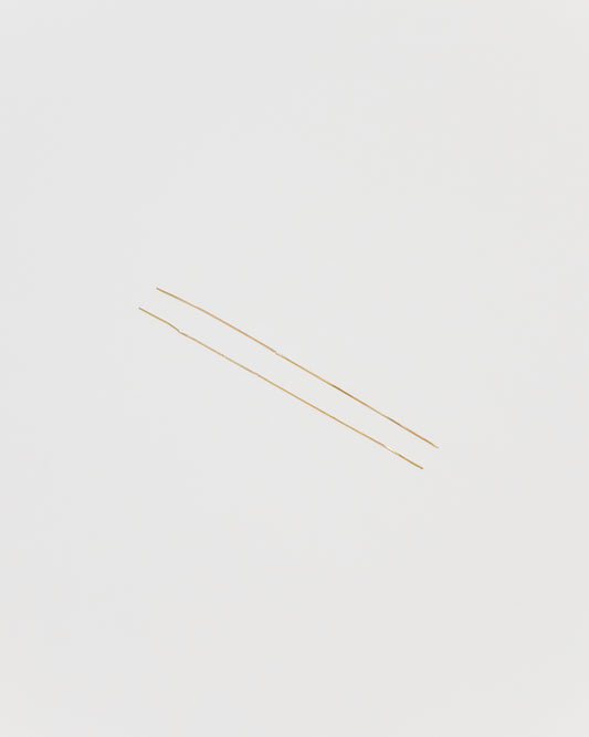 Two extremely thin gold chain strands laid diagonally on a solid light gray background.