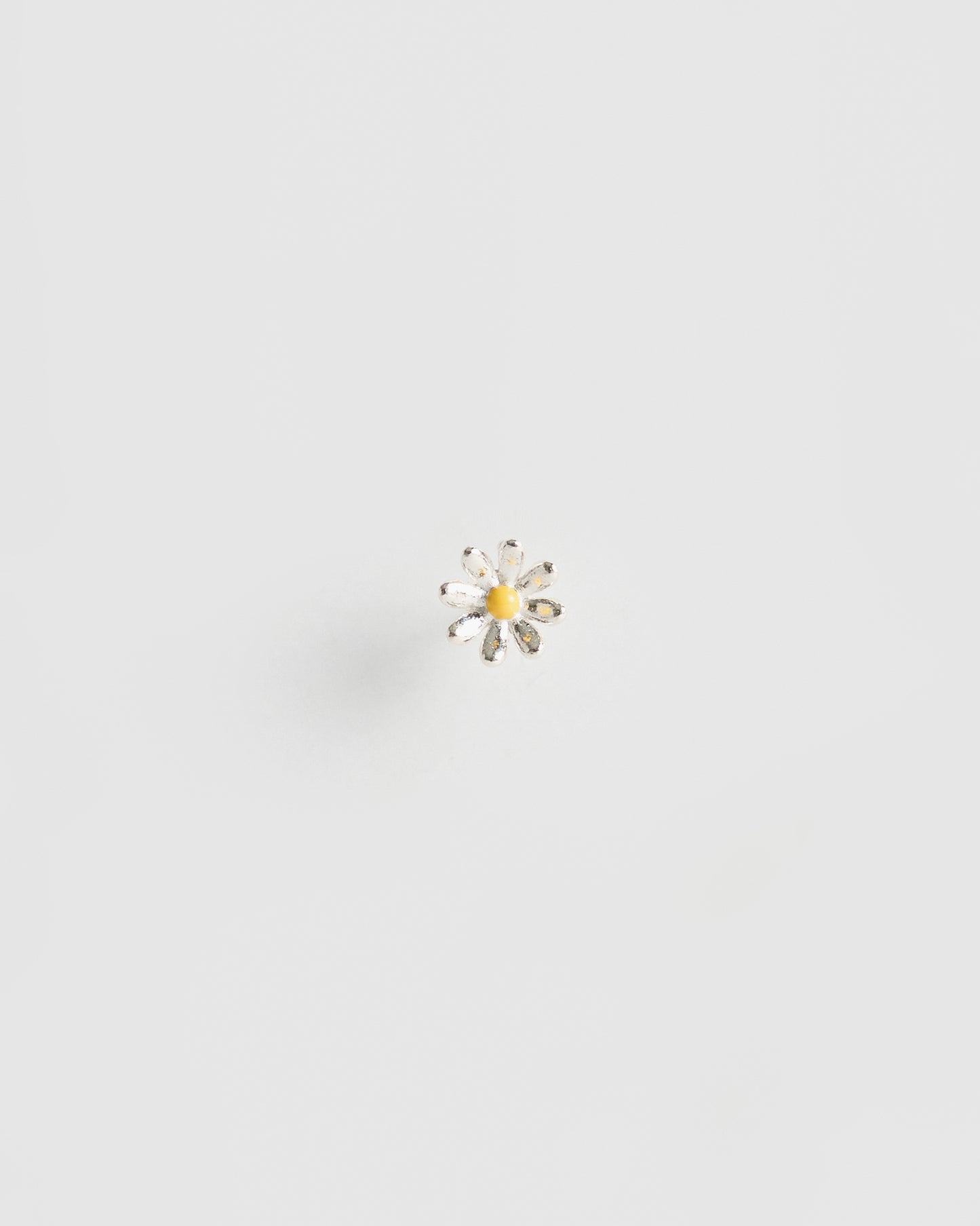 Small daisy-shaped stud earring in polished silver with rounded petal tips and a glossy yellow enamel center, placed alone on a clean white background.