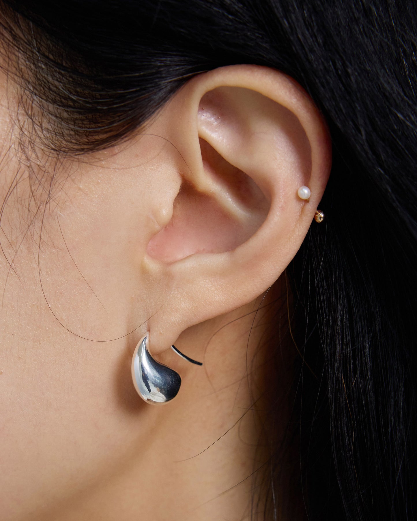 Close-up of silver organic drop earrings on ear, glossy curved statement piece