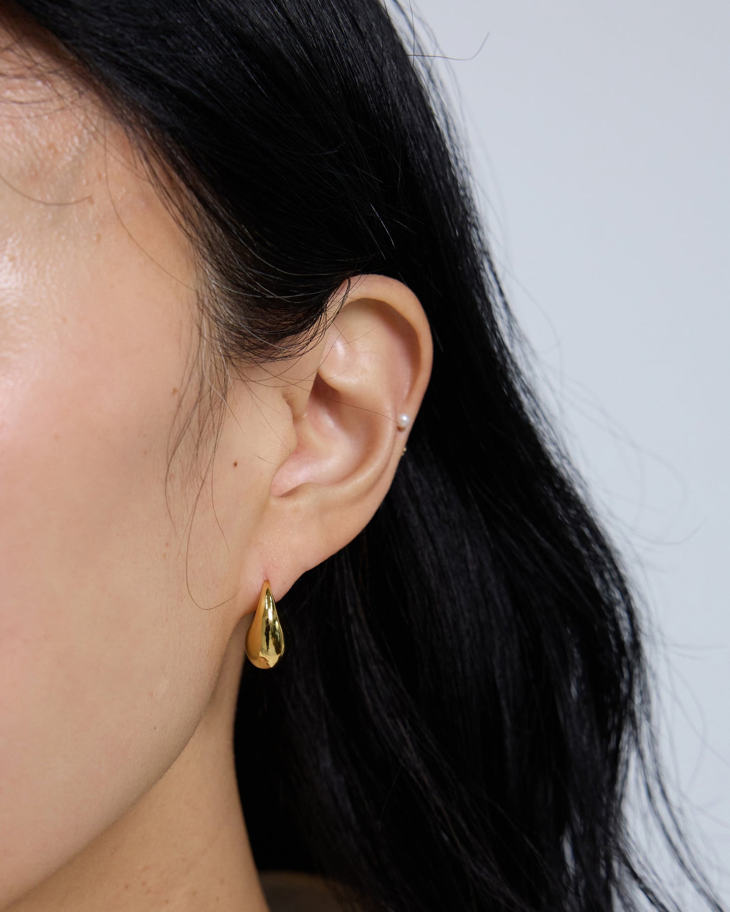 Profile view of a woman wearing the HANNA543 gold bold teardrop earring, highlighting the elegant satin finish and fluid shape.