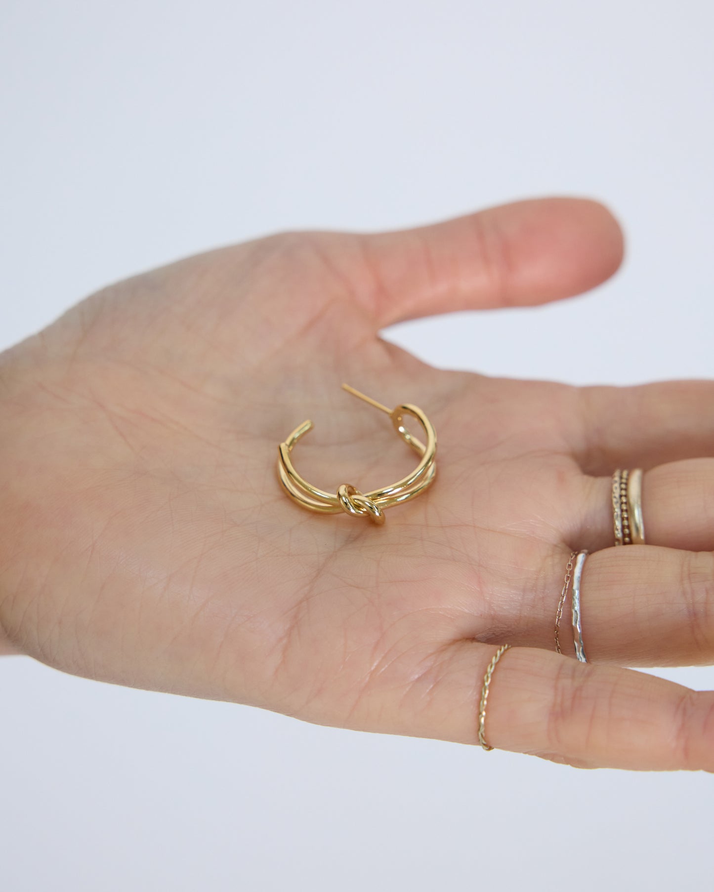 gold knot hoop earrings on hand size reference minimal gold jewelry detail everyday wearable earrings