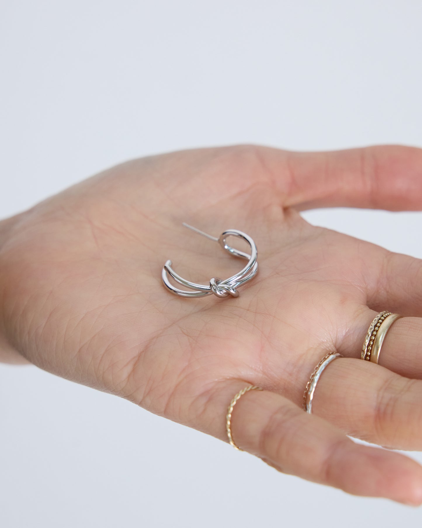 silver knot hoop earrings on hand minimal jewelry detail modern everyday silver earrings size reference