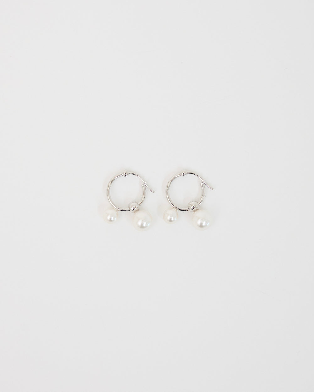 silver hoop earrings with two pearl drops on white surface