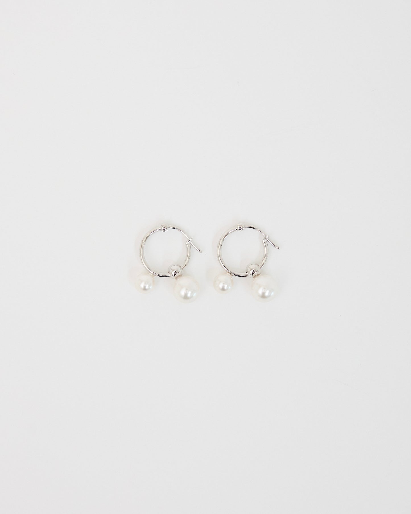 silver hoop earrings with two pearl drops on white surface