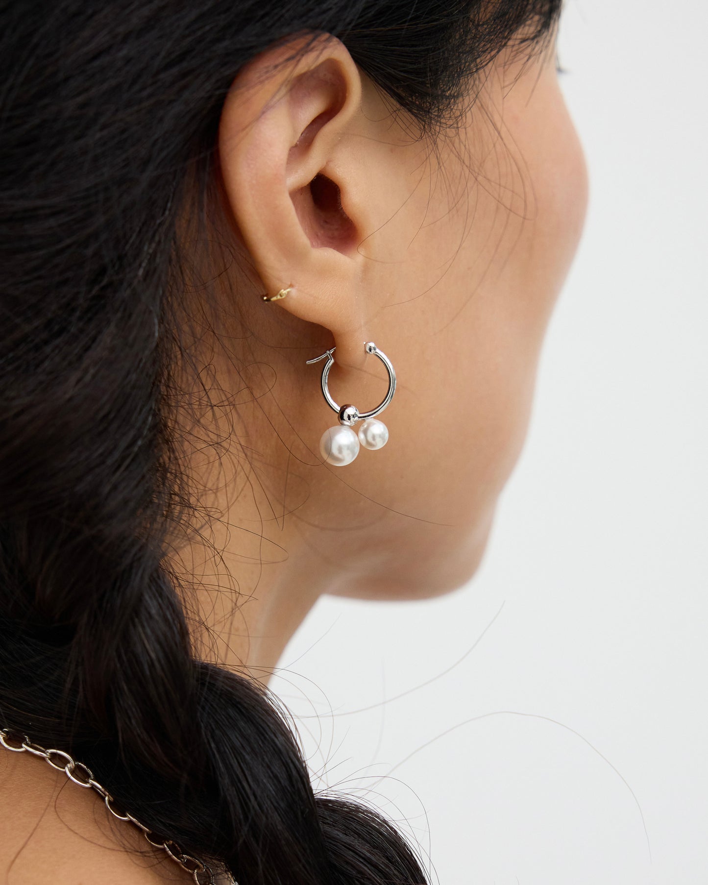 Rear side angle of a model wearing silver-tone hoop earrings with two white pearl drops, emphasizing the pearl placement and open circular hoop design.