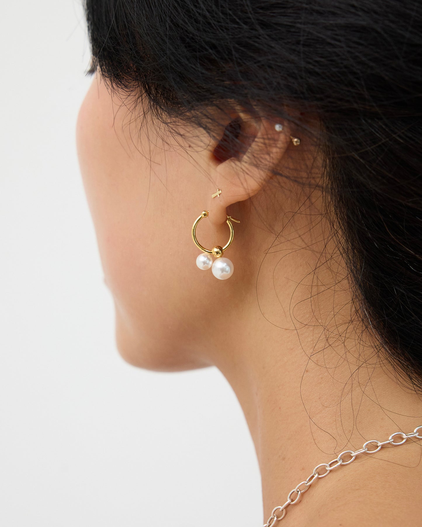 Rear side view of a model wearing gold-tone hoop earrings with two white pearl drops, showing how the pearls sit just below the earlobe.