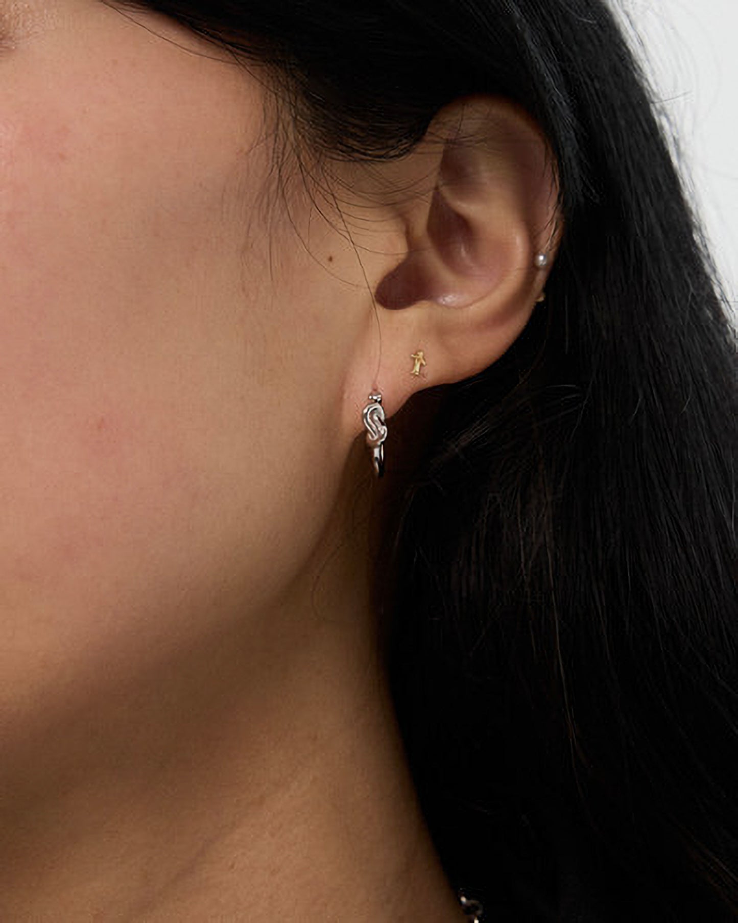 Close-up of an ear with two earrings on a neutral background