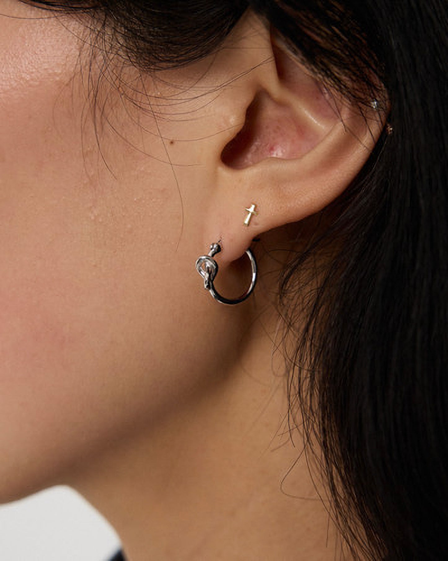 Close-up of an ear with a silver hoop earring and a small stud.