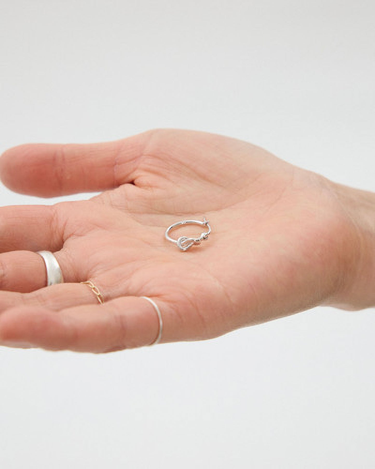 Hand wearing multiple silver rings on a light gray background