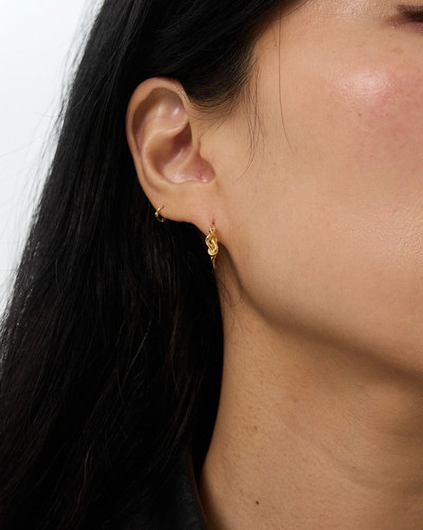 Close-up of a person wearing gold hoop earrings with a plain background