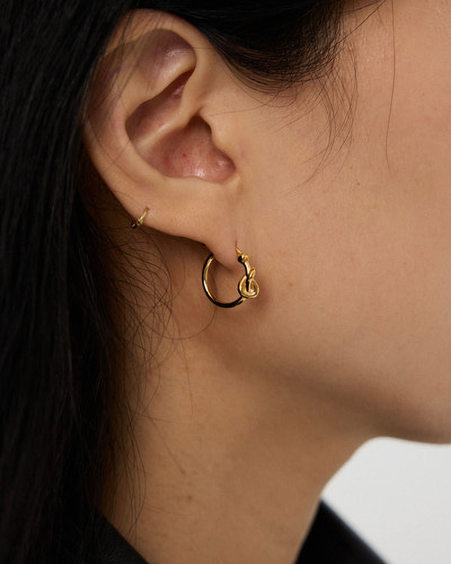 Close-up of an ear wearing a gold hoop earring with a small pendant.