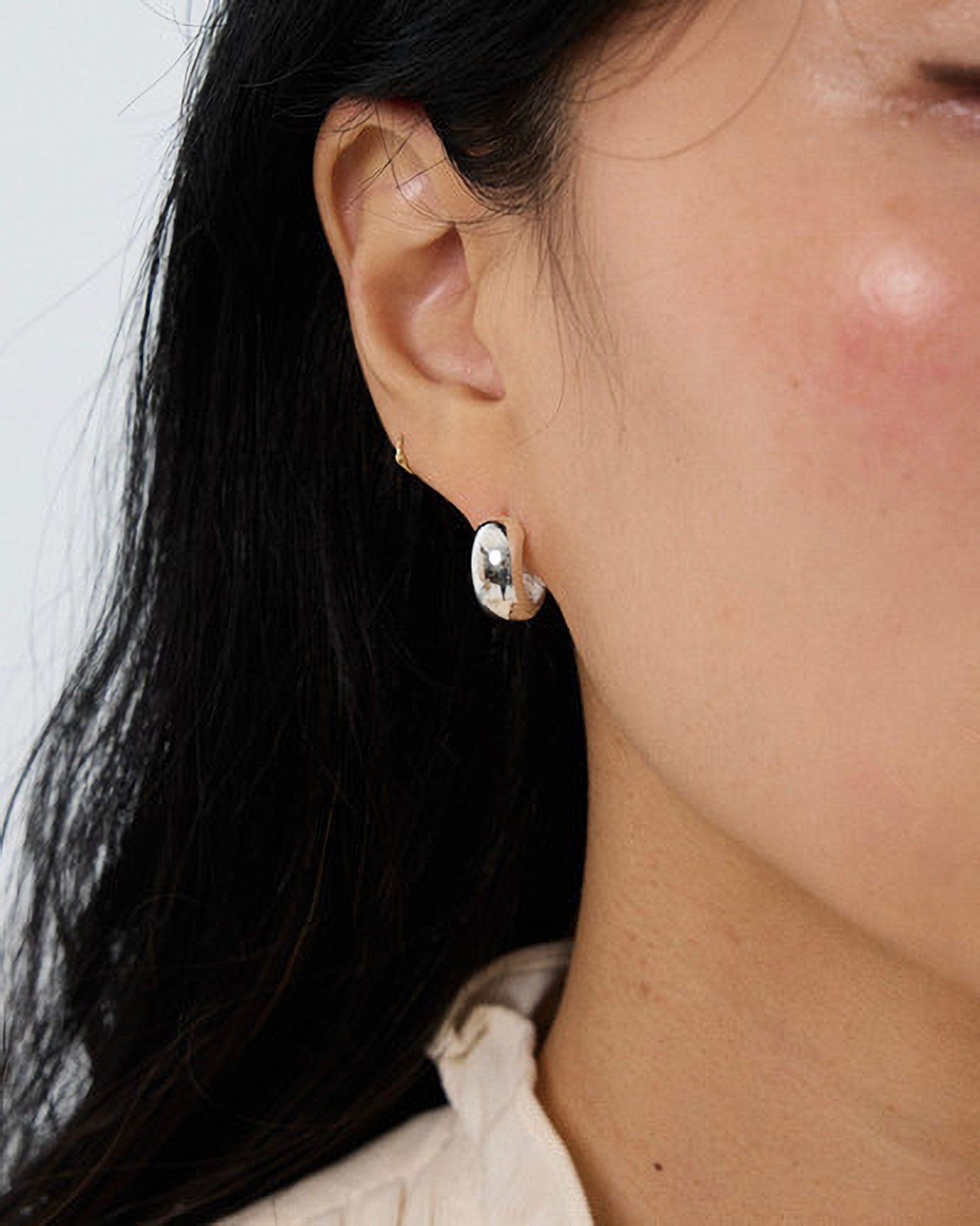 Close-up of an ear wearing a small hoop earring with a plain background