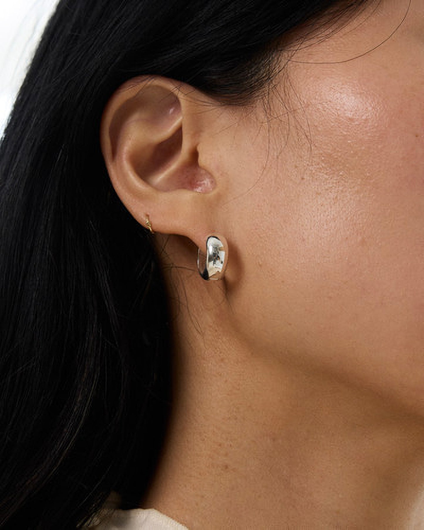 Close-up of an ear wearing a silver earring with a clear gemstone.