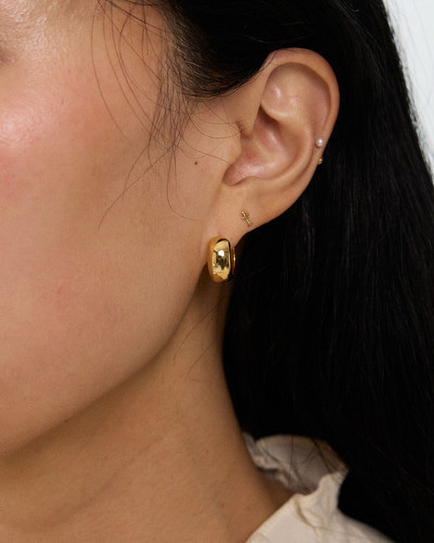Close-up of an ear wearing gold hoop earrings with a dark background