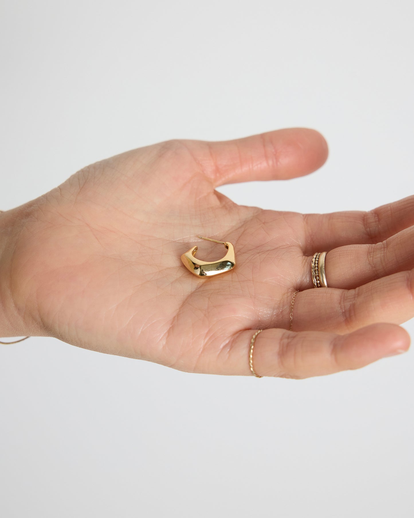 gold sculptural hoop earring held in hand, curved bold gold earring detail, polished surface jewelry