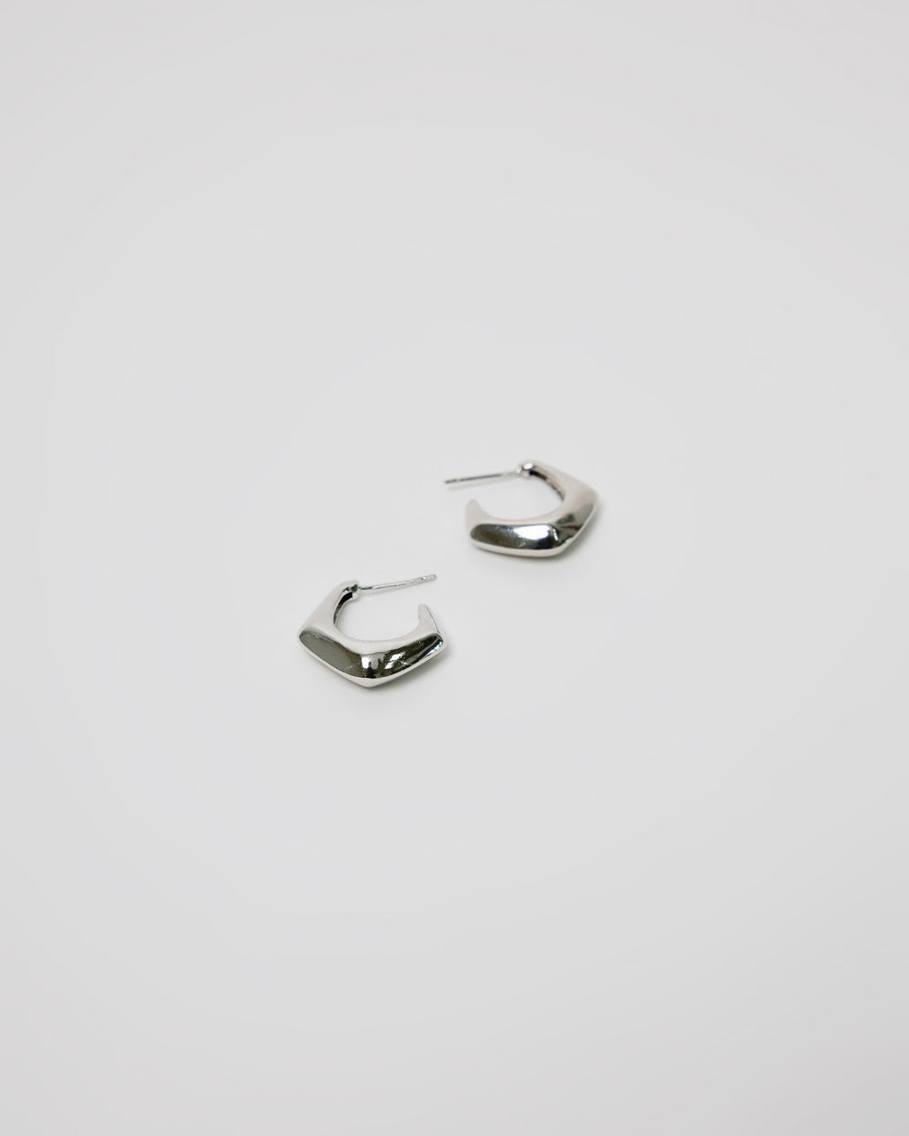 pair of silver curved hoop earrings on white background, bold minimal jewelry design
