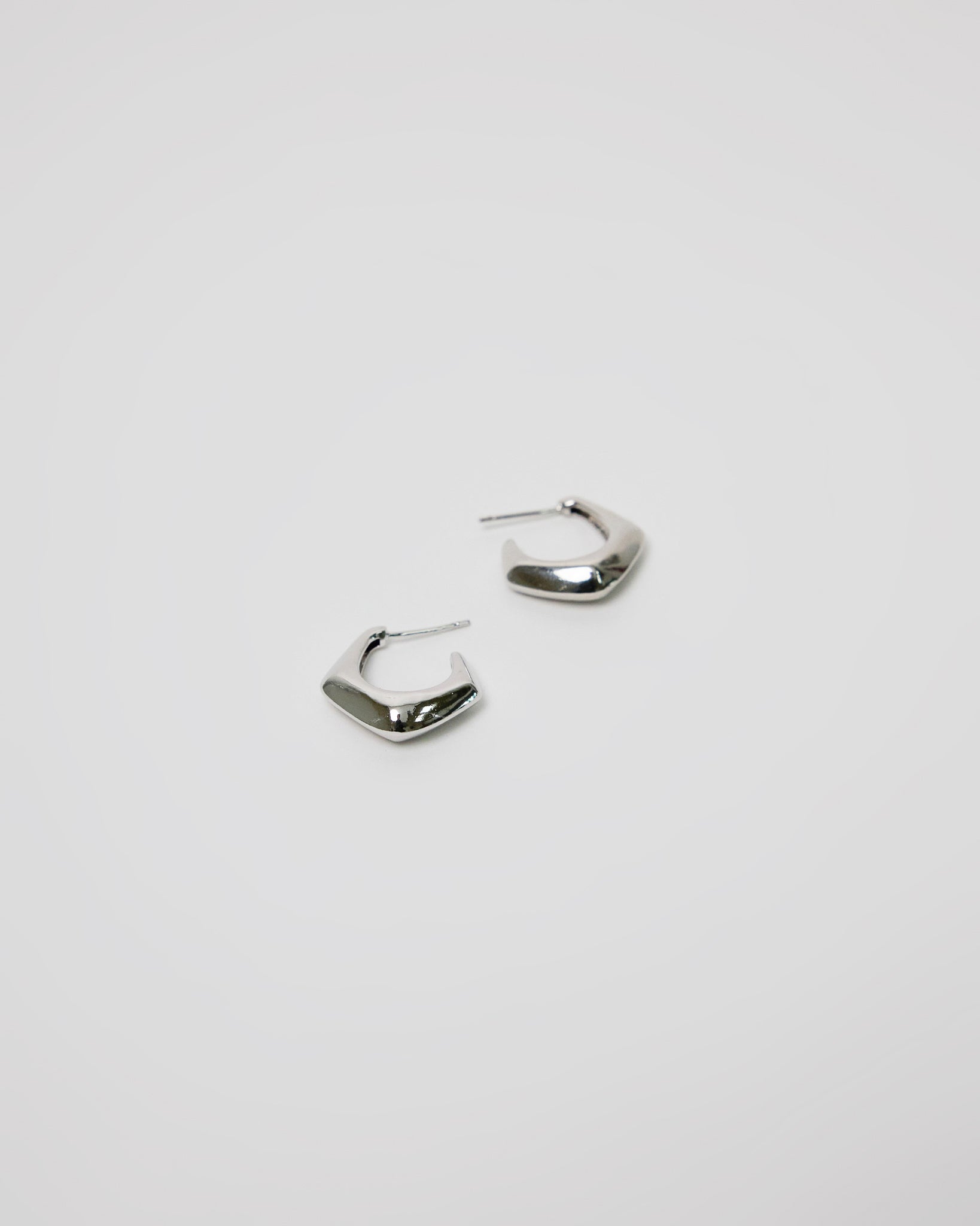 pair of silver curved hoop earrings on white background, bold minimal jewelry design