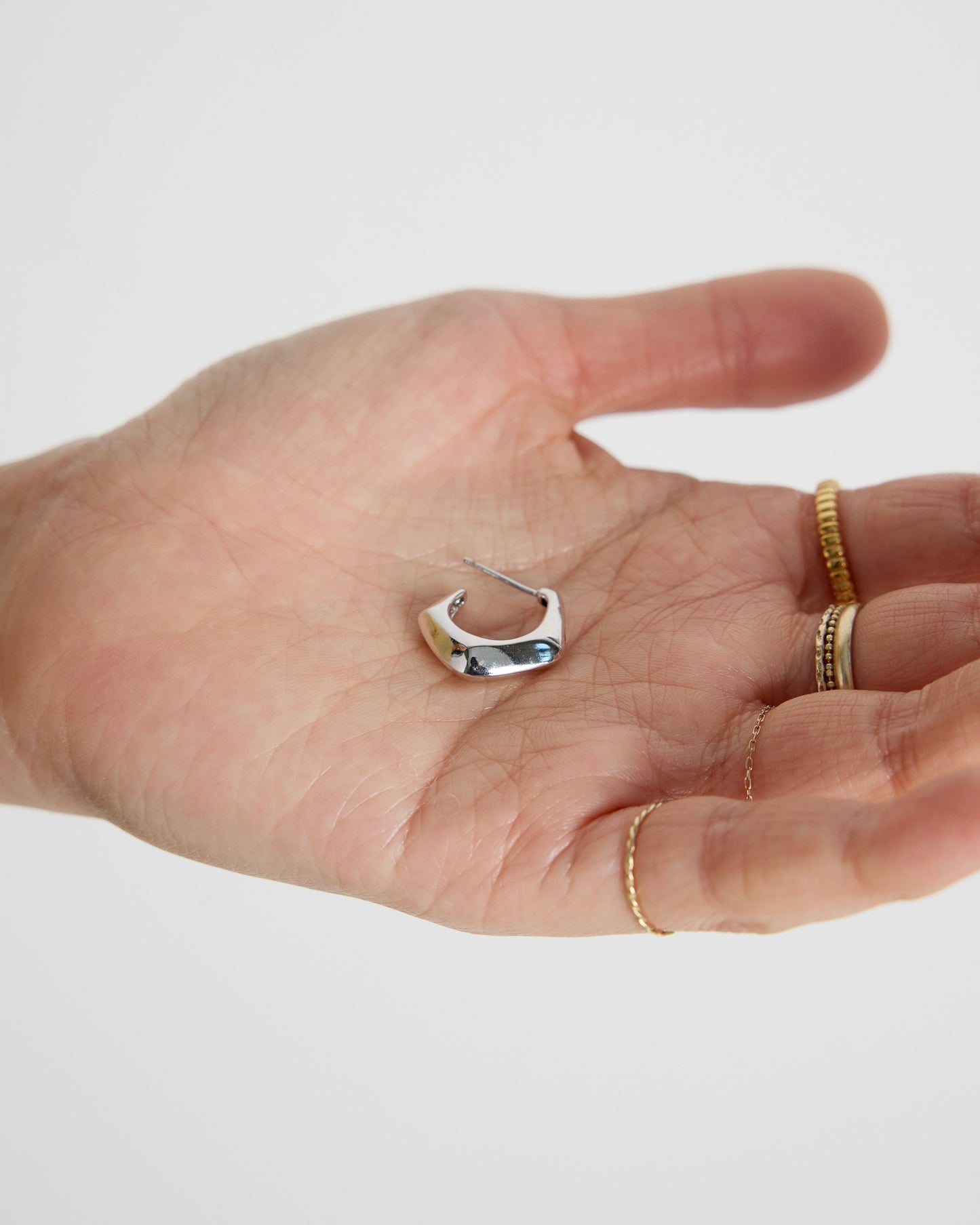 silver curved hoop earring held in hand, polished sculptural silver jewelry detail