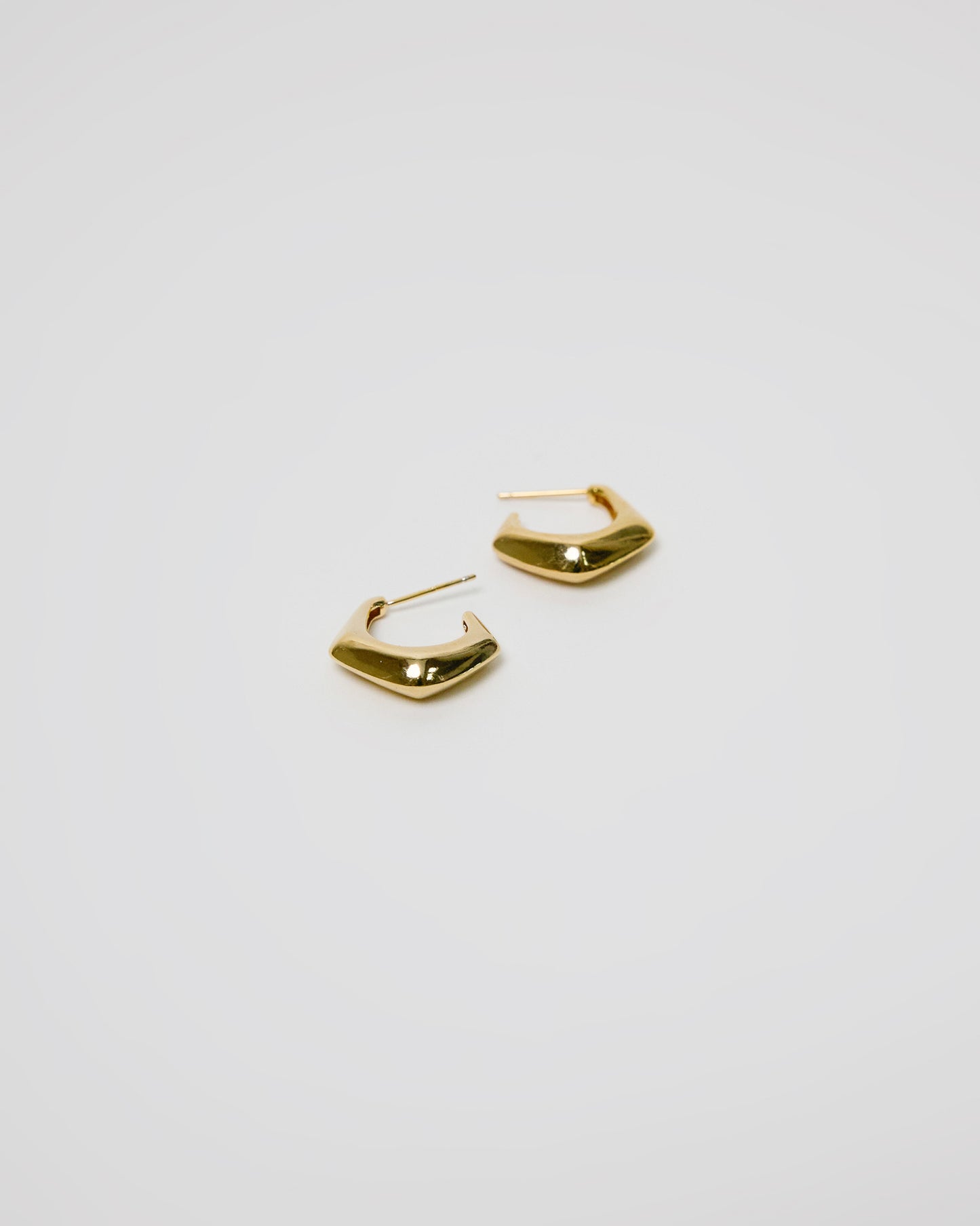 pair of gold sculptural hoop earrings on white background, bold curved shape jewelry