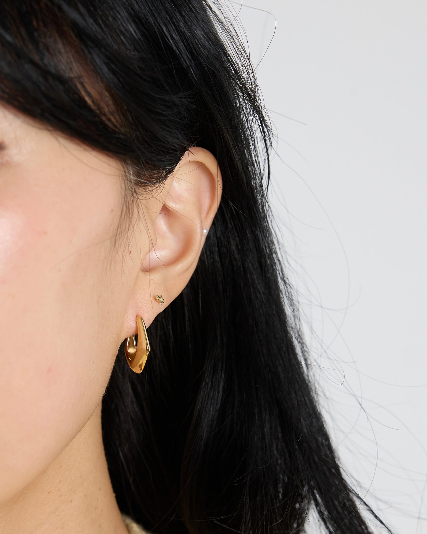 gold chunky curved hoop earrings worn on ear, minimalist sculptural gold earrings, modern everyday jewelry styling