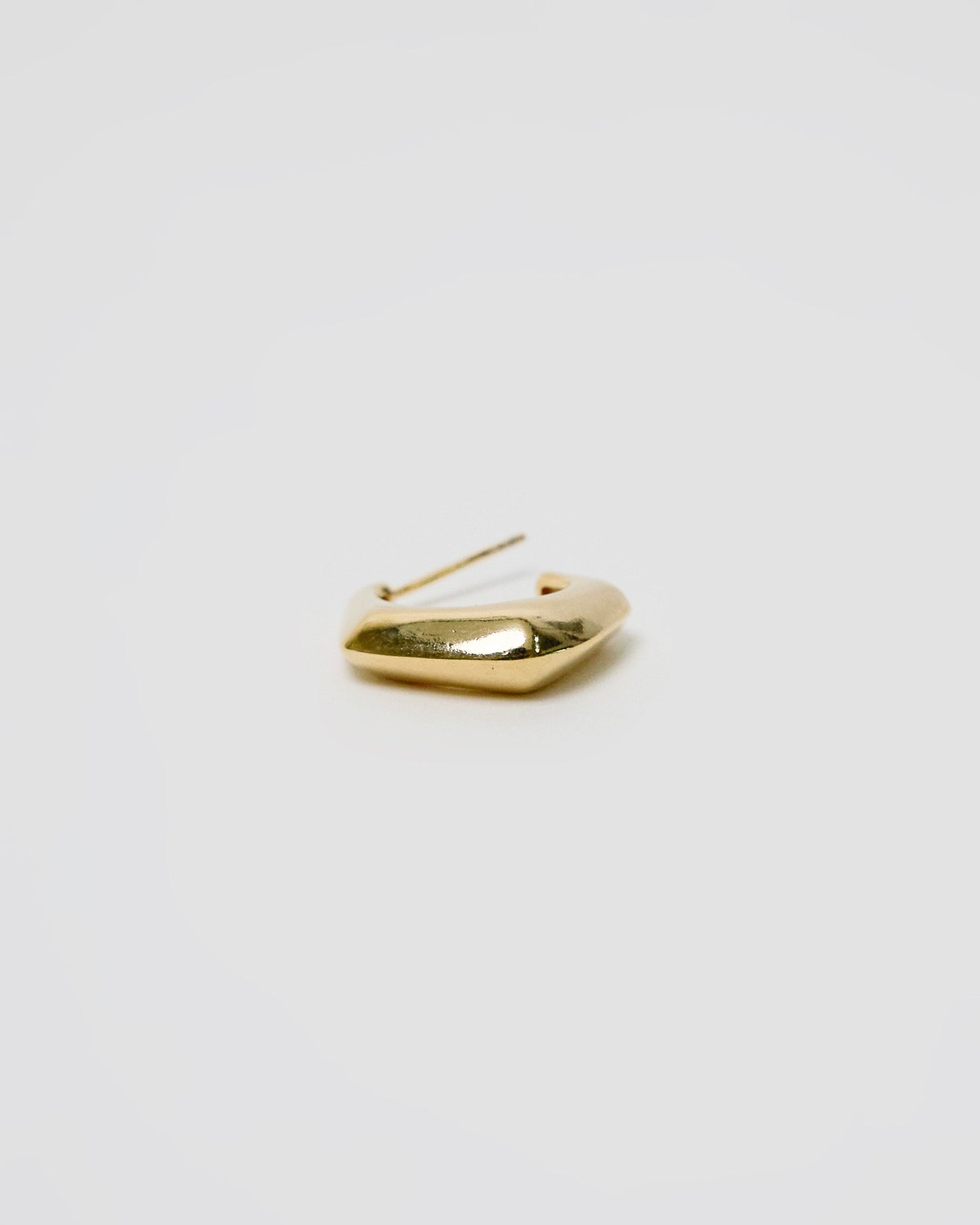 close up of gold curved hoop earring showing smooth reflective surface and sculptural form