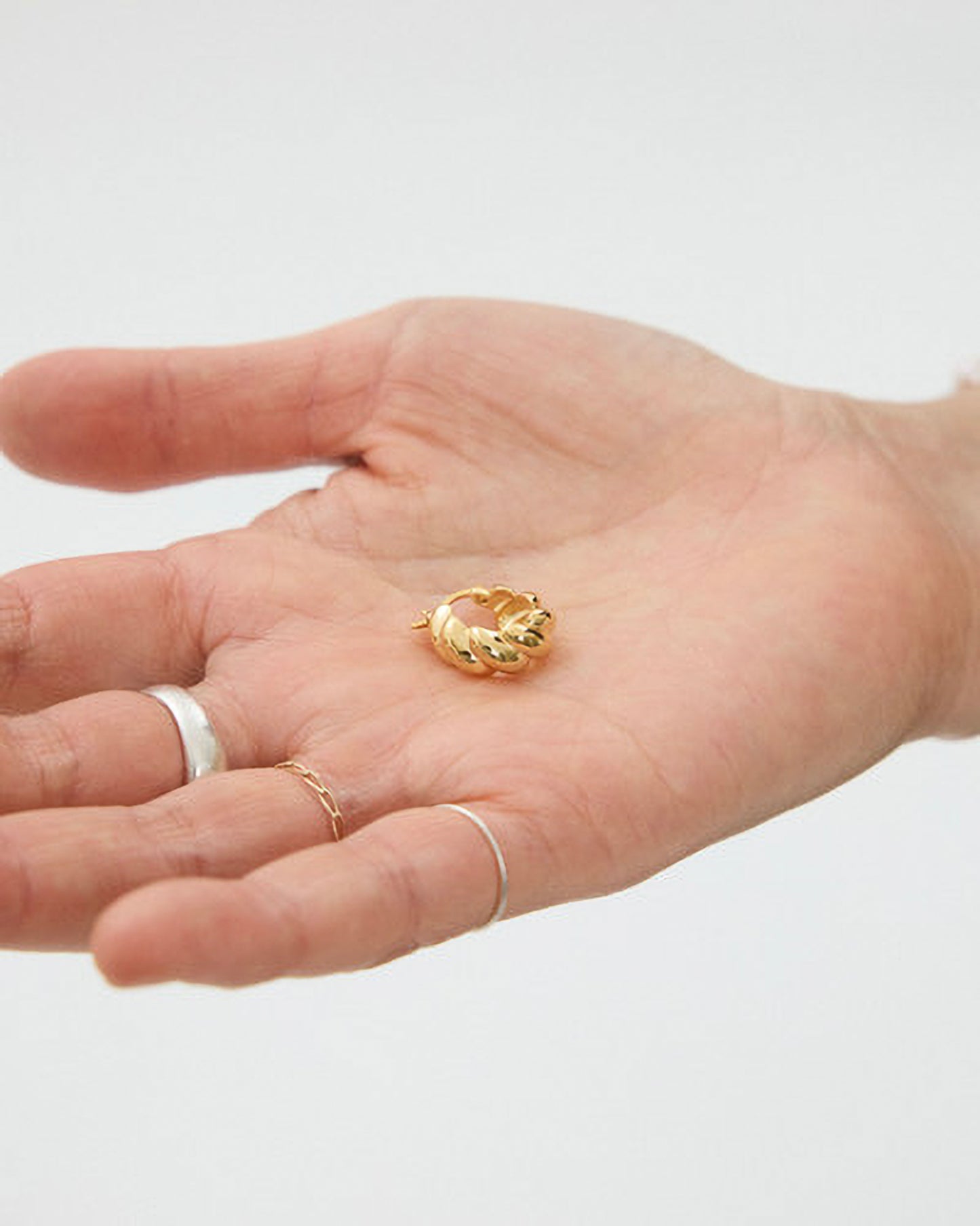 Hand holding a gold ring on a plain background