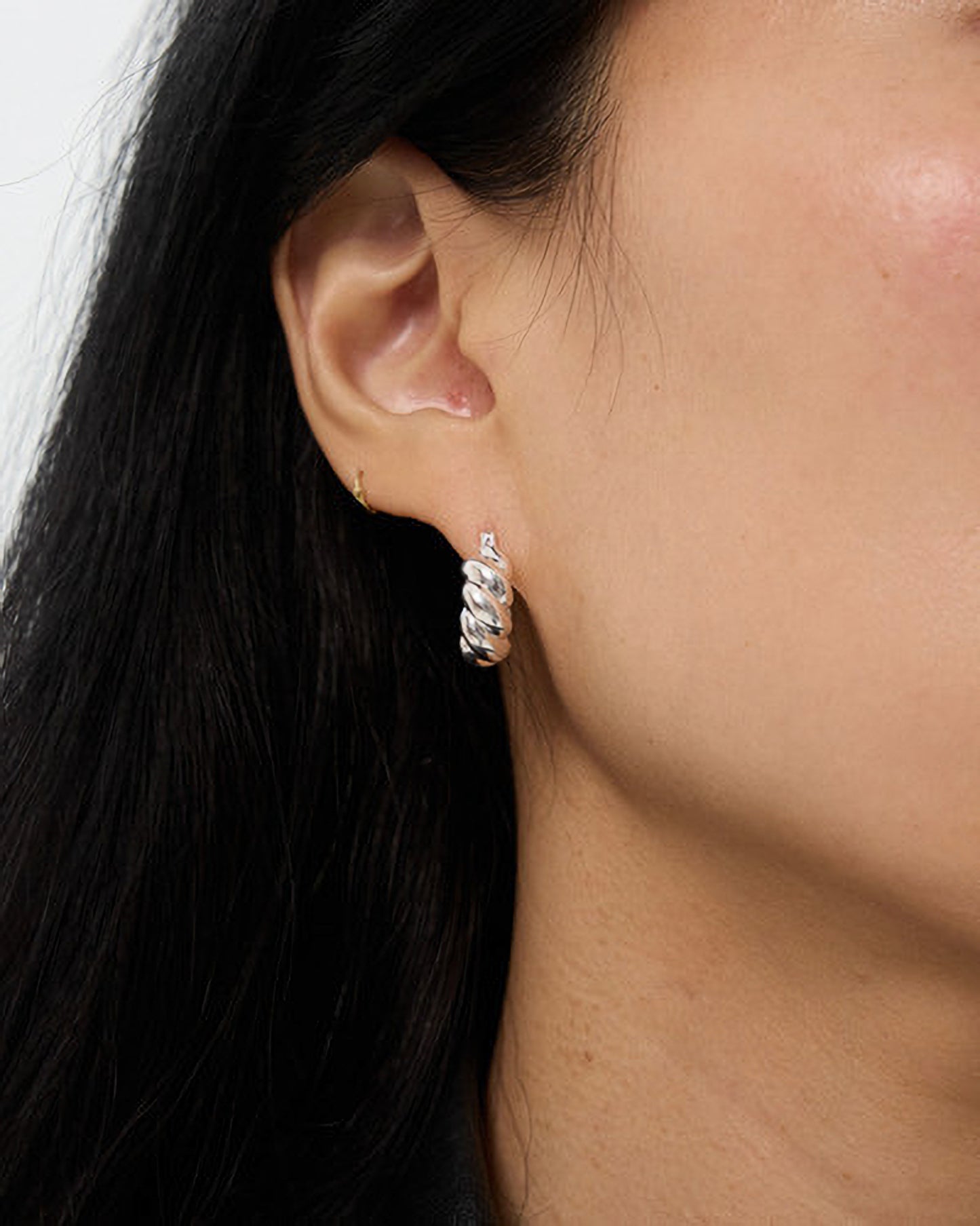 Close-up of an ear wearing a silver hoop earring with dark hair and skin visible.