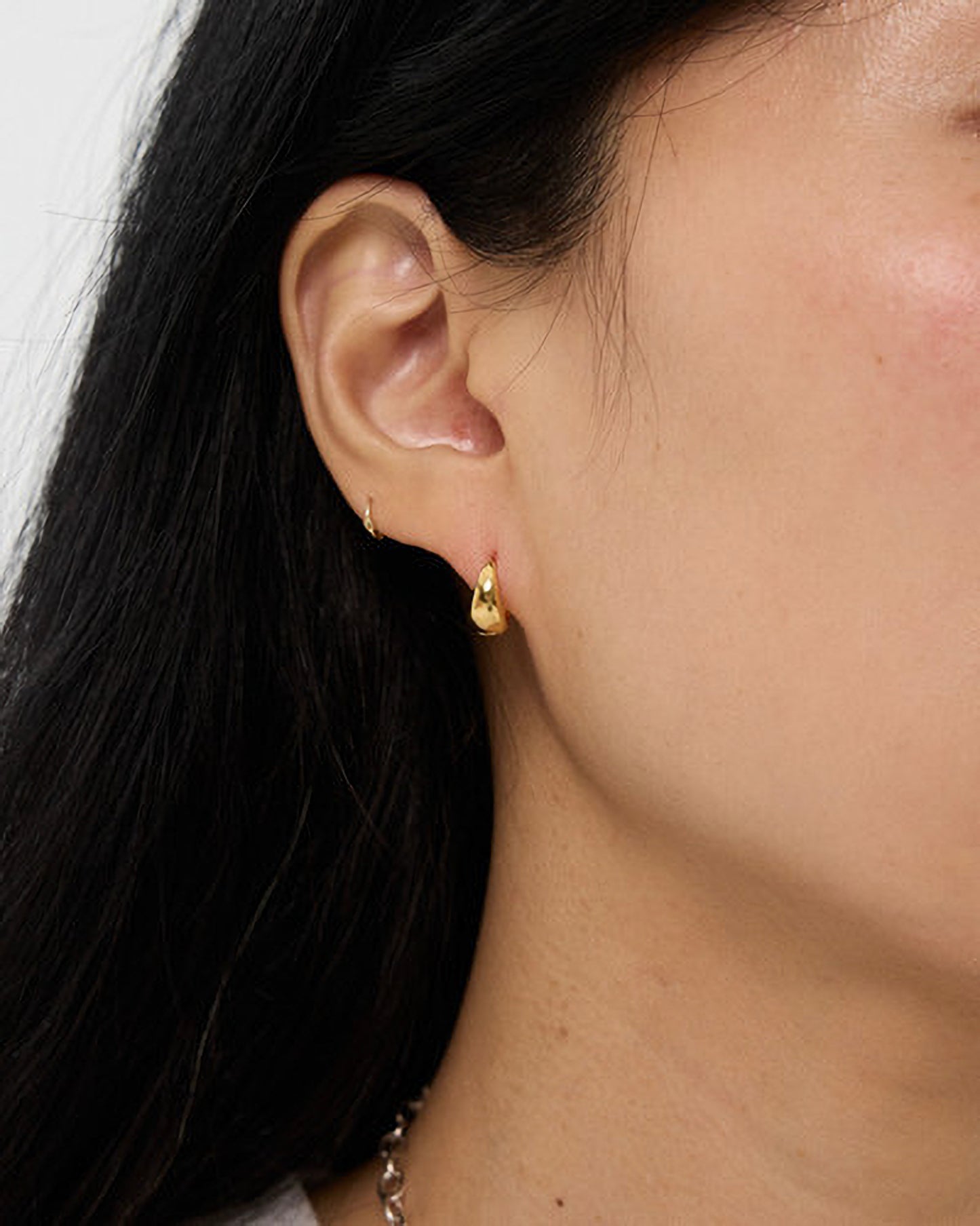 Close-up of an ear wearing a gold earring with dark hair and skin visible.