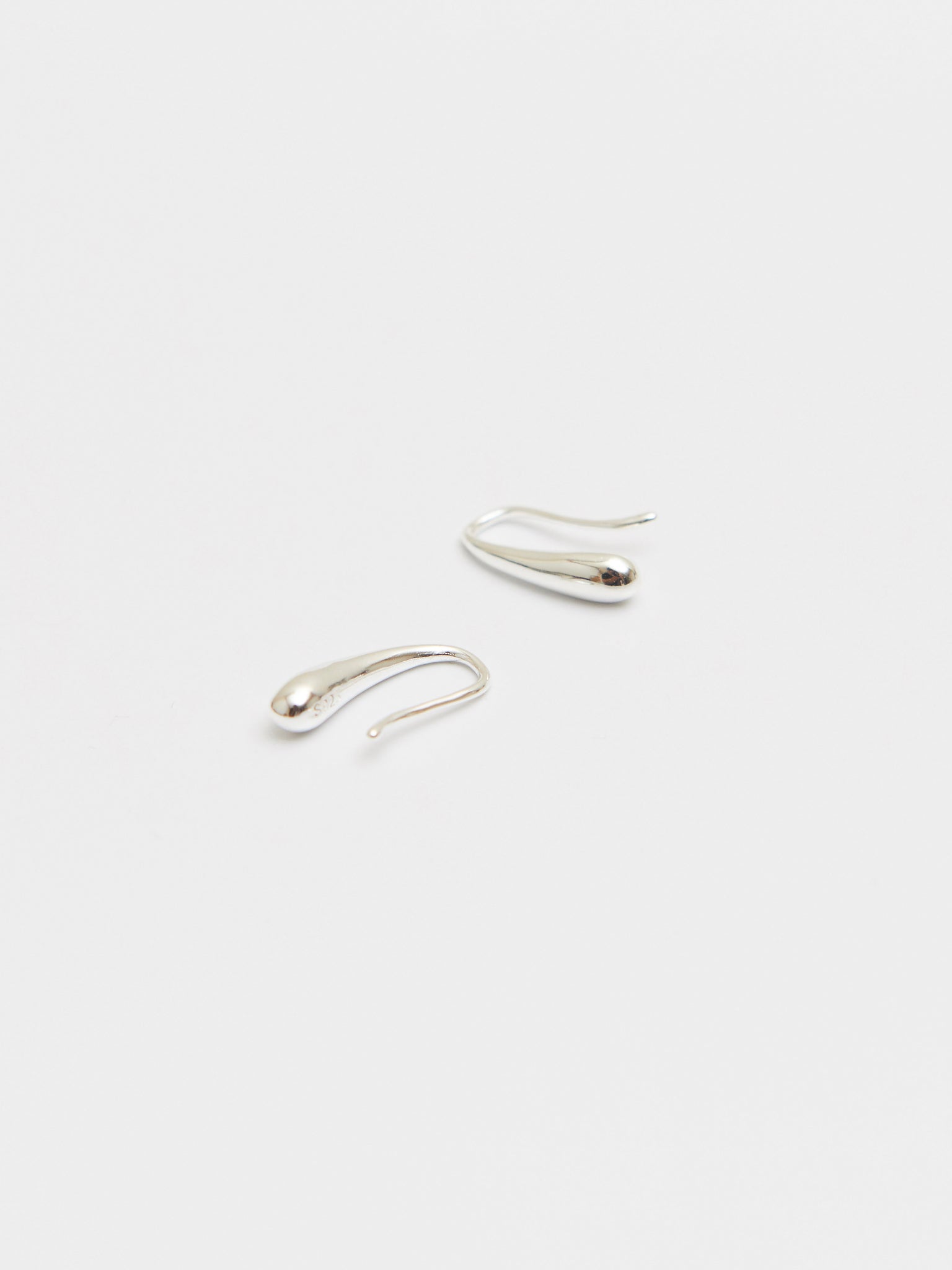 This image displays a pair of elegant silver teardrop hooks, crafted from high-quality 925 sterling silver. Originating from Korea, these hooks are designed with a minimalist and modern aesthetic, emphasizing natural raw materials and timeless allure.