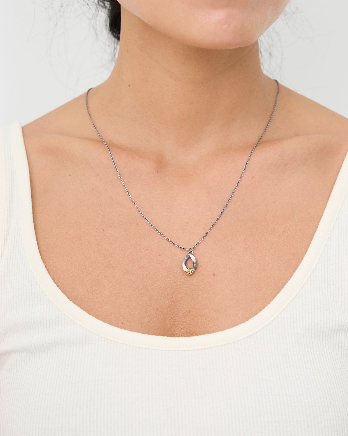 Woman wearing a sterling antique silver and gold mixed metal pendant necklace with white tank top