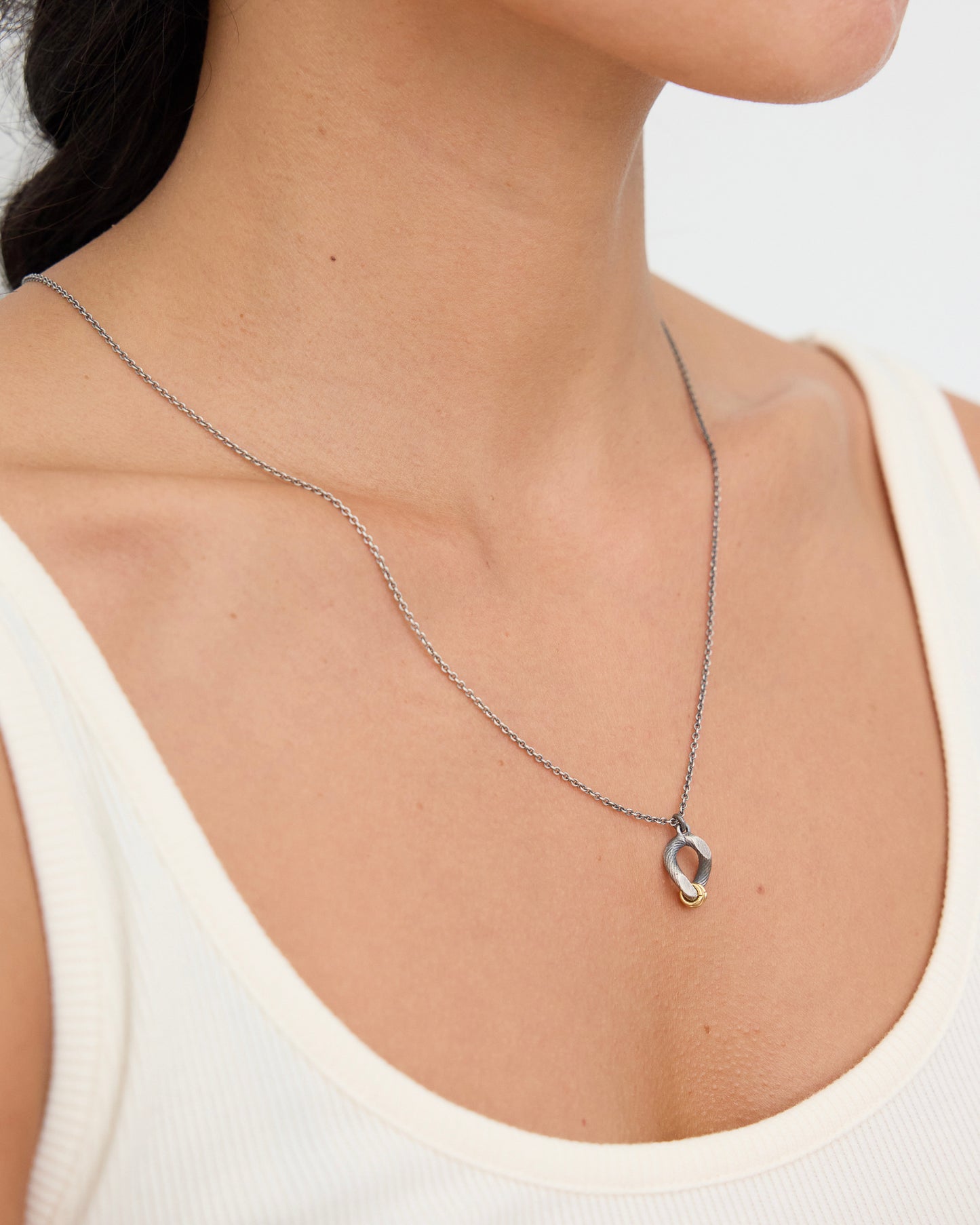 Side profile view of a woman wearing a sculptural mixed metal pendant necklace