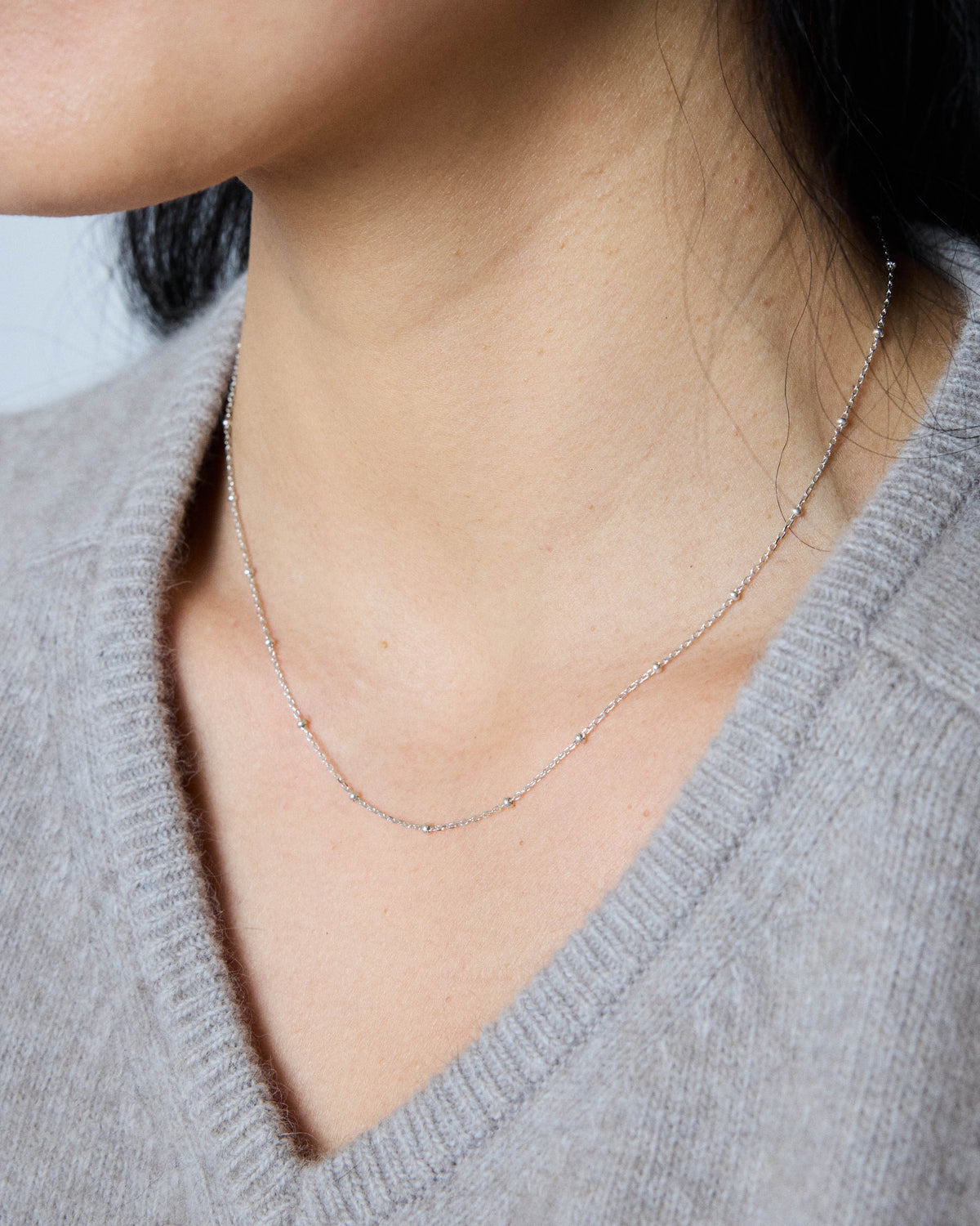 Model wearing a dainty silver ball station chain necklace with a gray V-neck sweater – HANNA543 N1057 starlit dot chain