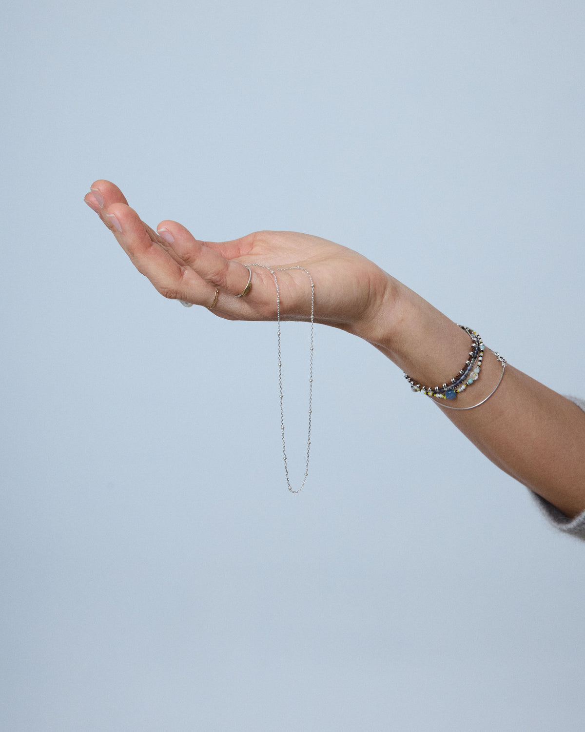 Hand holding a silver dot chain necklace against a soft blue background – HANNA543 N1057 starlit dot chain